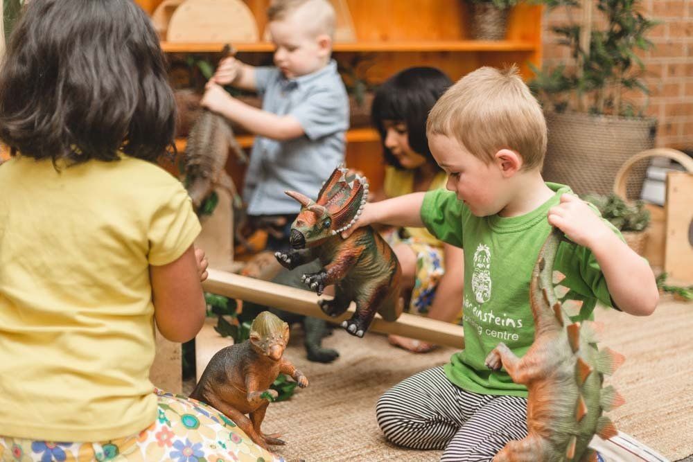 A group of children are playing with toy dinosaurs on the floor.