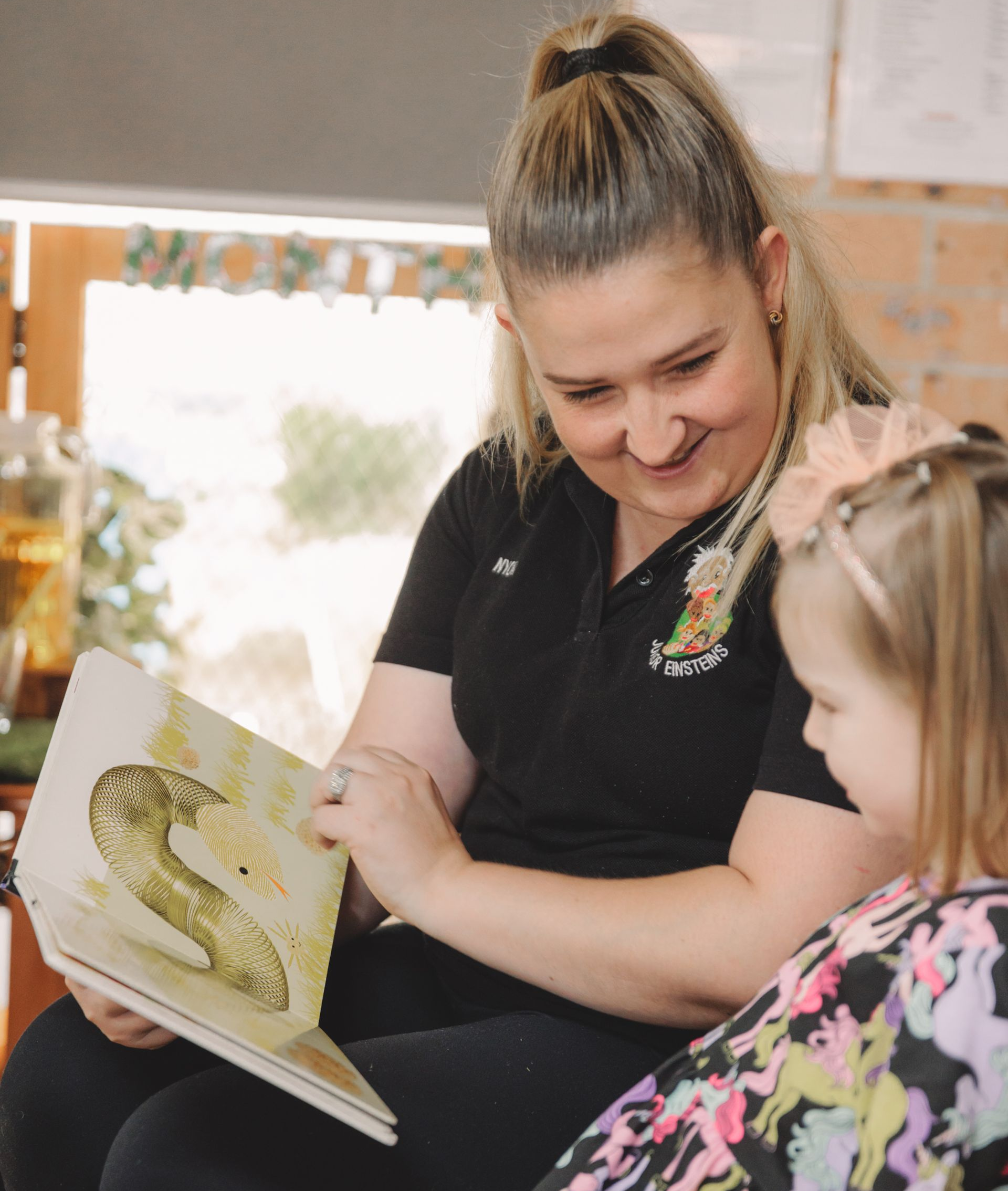 Woman reads to a young child from a book. Both are smiling, in an indoor setting. Woman reads to a young child from a book. Both are smiling, in an indoor setting.
