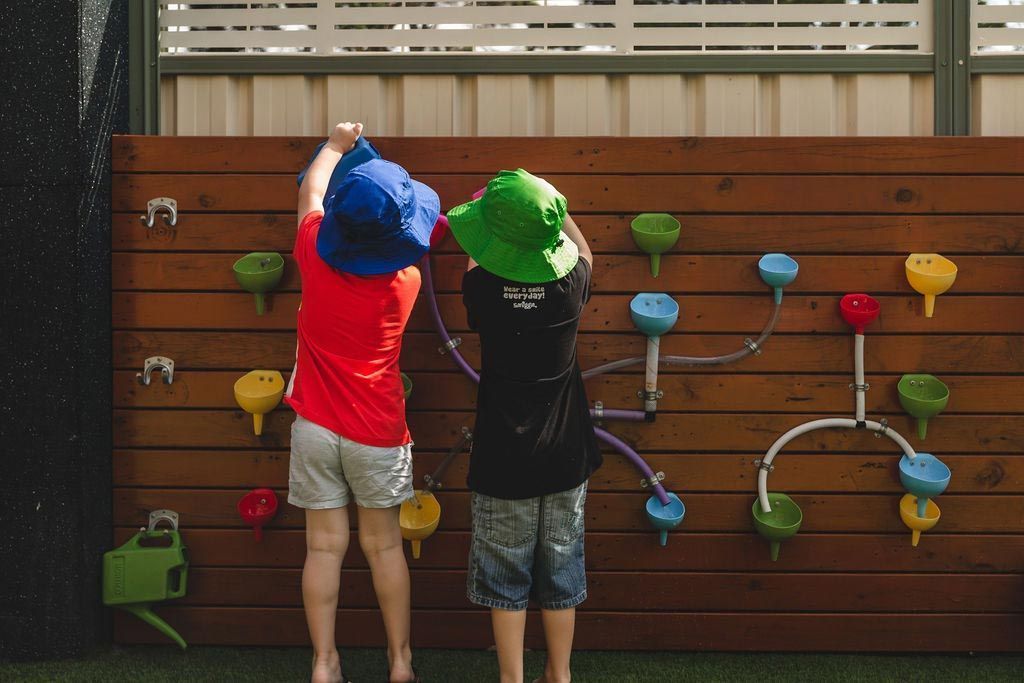 Two children are standing in front of a climbing wall.