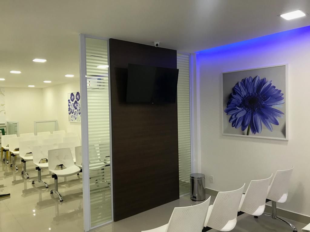 Uma sala de espera com cadeiras brancas e uma flor azul na parede.