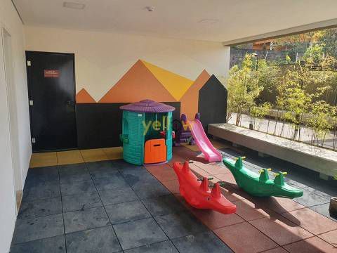 Um playground com escorregador, balanços e uma casa.