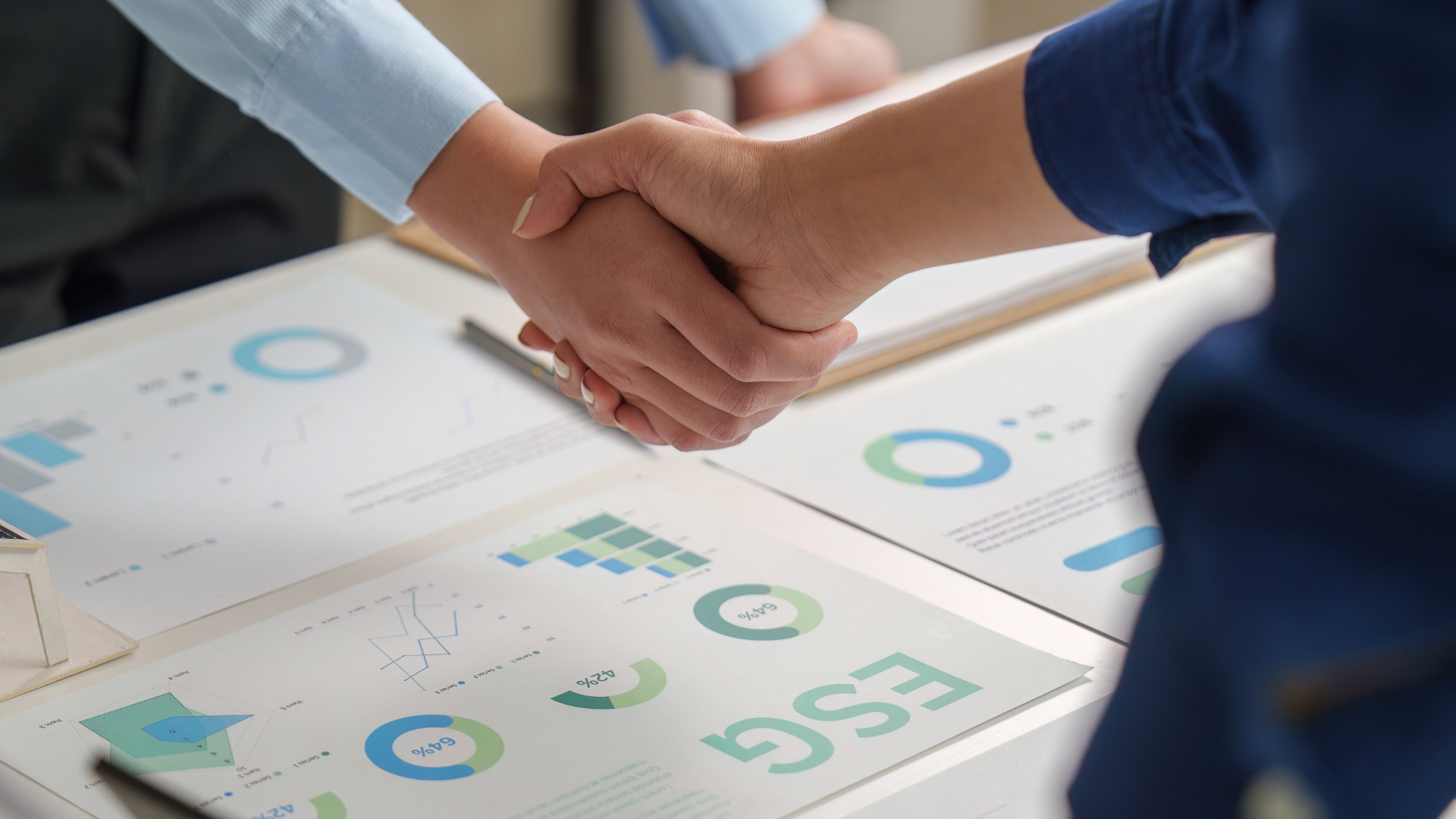 Two people shaking hands over business charts and graphs on a desk