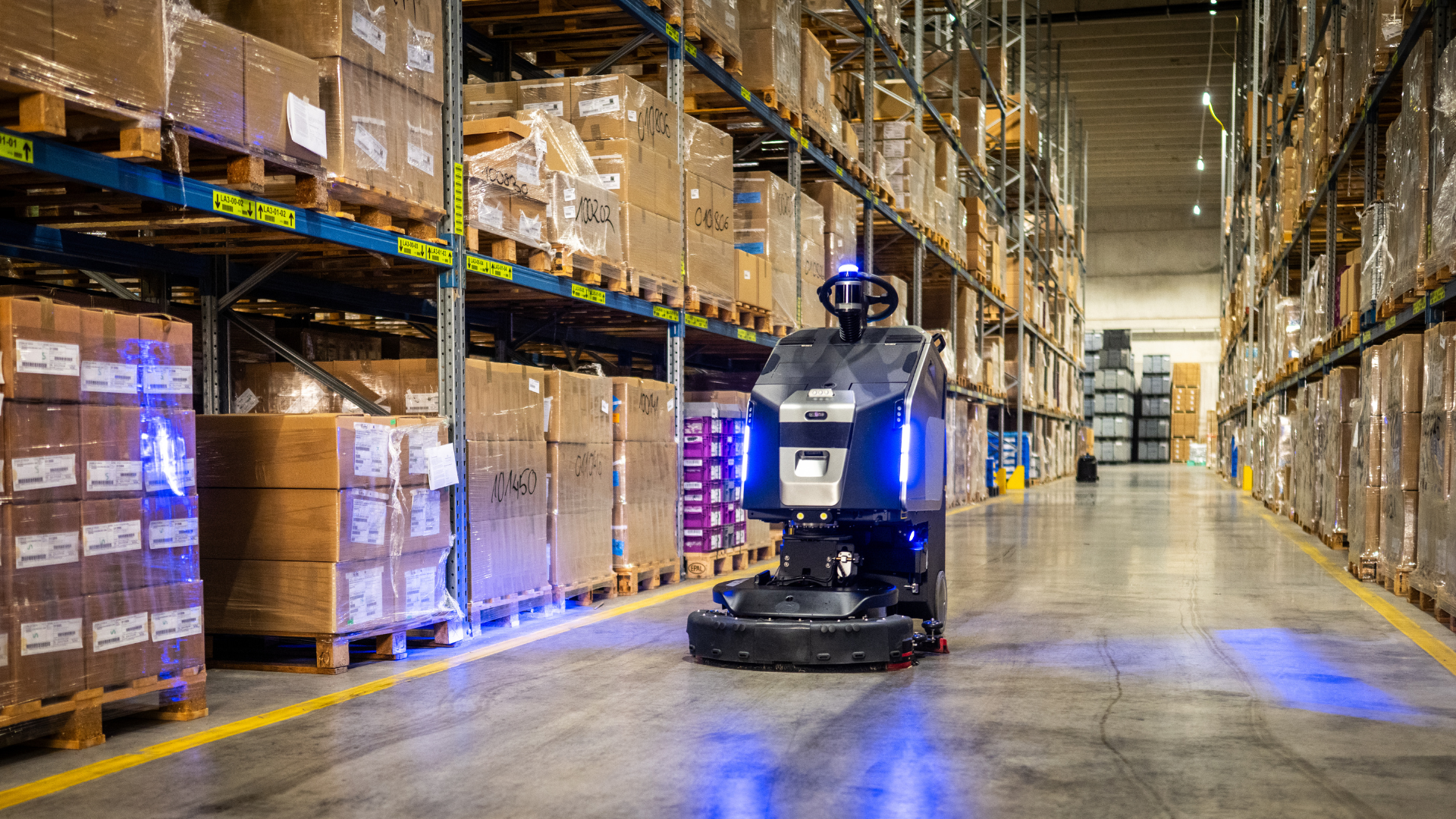 Autonomous robot moving through a warehouse aisle lined with stacked cardboard boxes