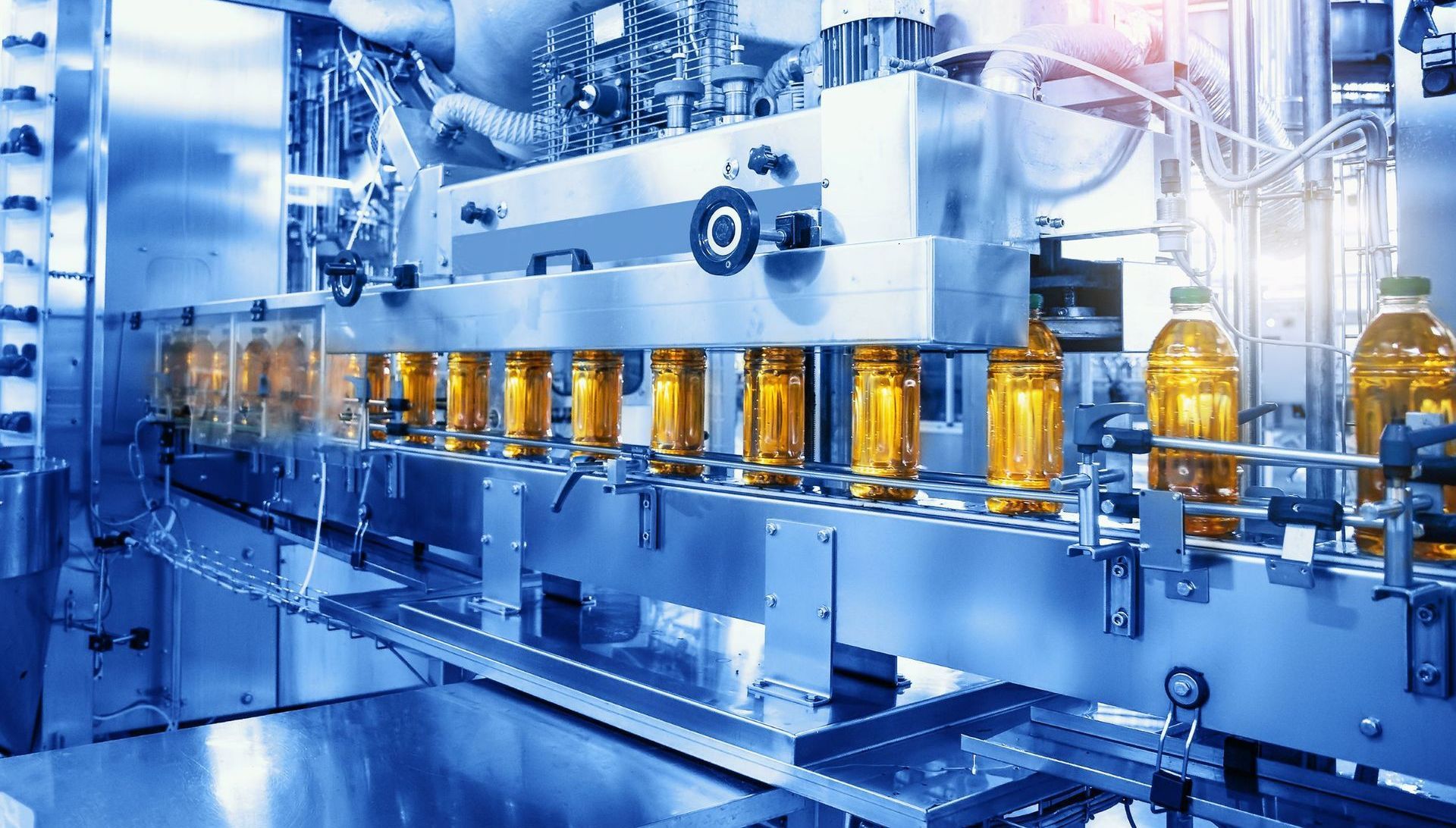 Bottles of golden liquid being filled on an automated production line in a factory.