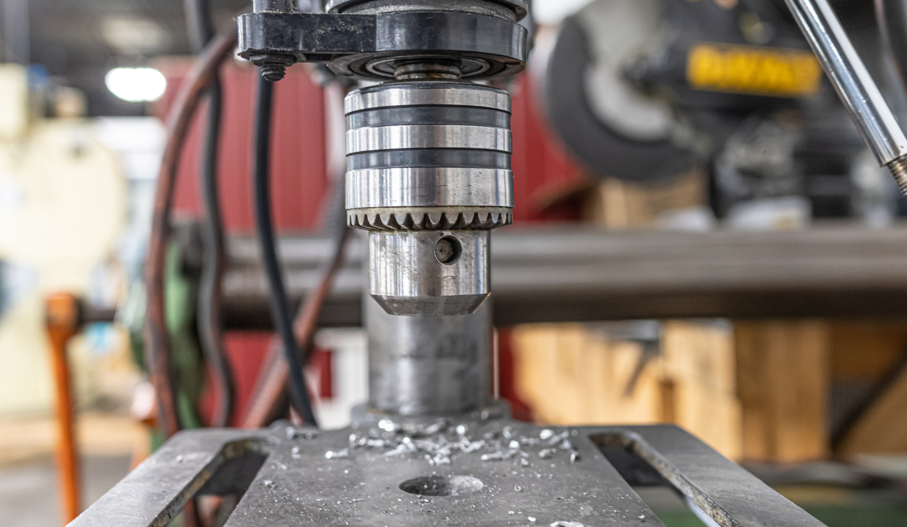 Close-up of a drill press with metal shavings on the work surface. The drill bit is in place, ready to drill.