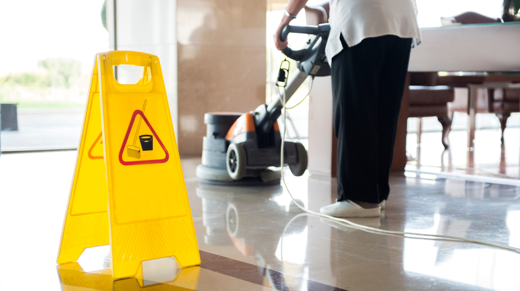 A person is cleaning a floor next to a yellow caution sign.