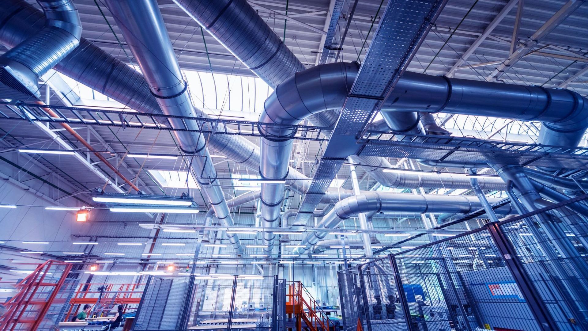 Industrial interior with large ventilation pipes, metal framework, and overhead lights.