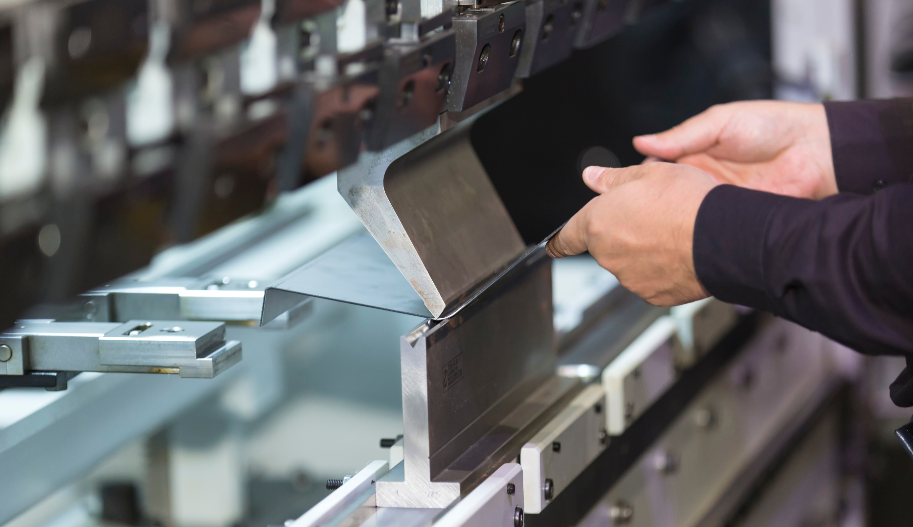 Hands bending metal sheet with an industrial machine.