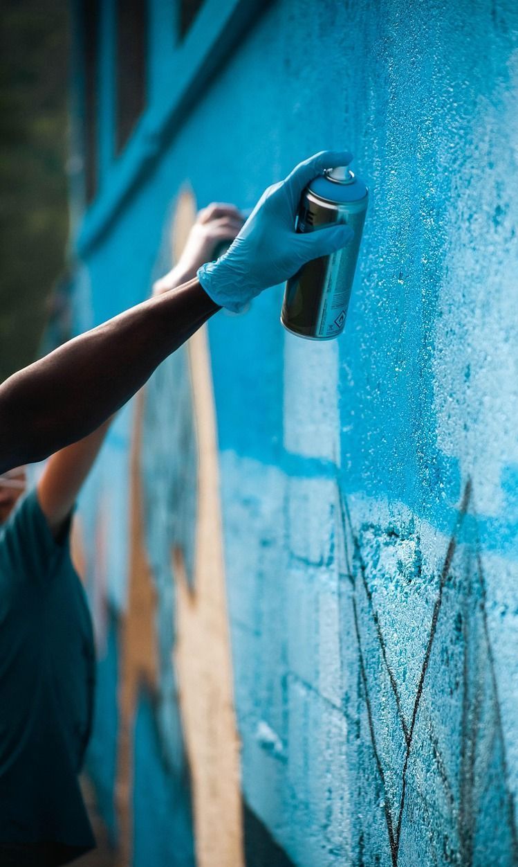 A person is spray painting a blue wall with a spray can.