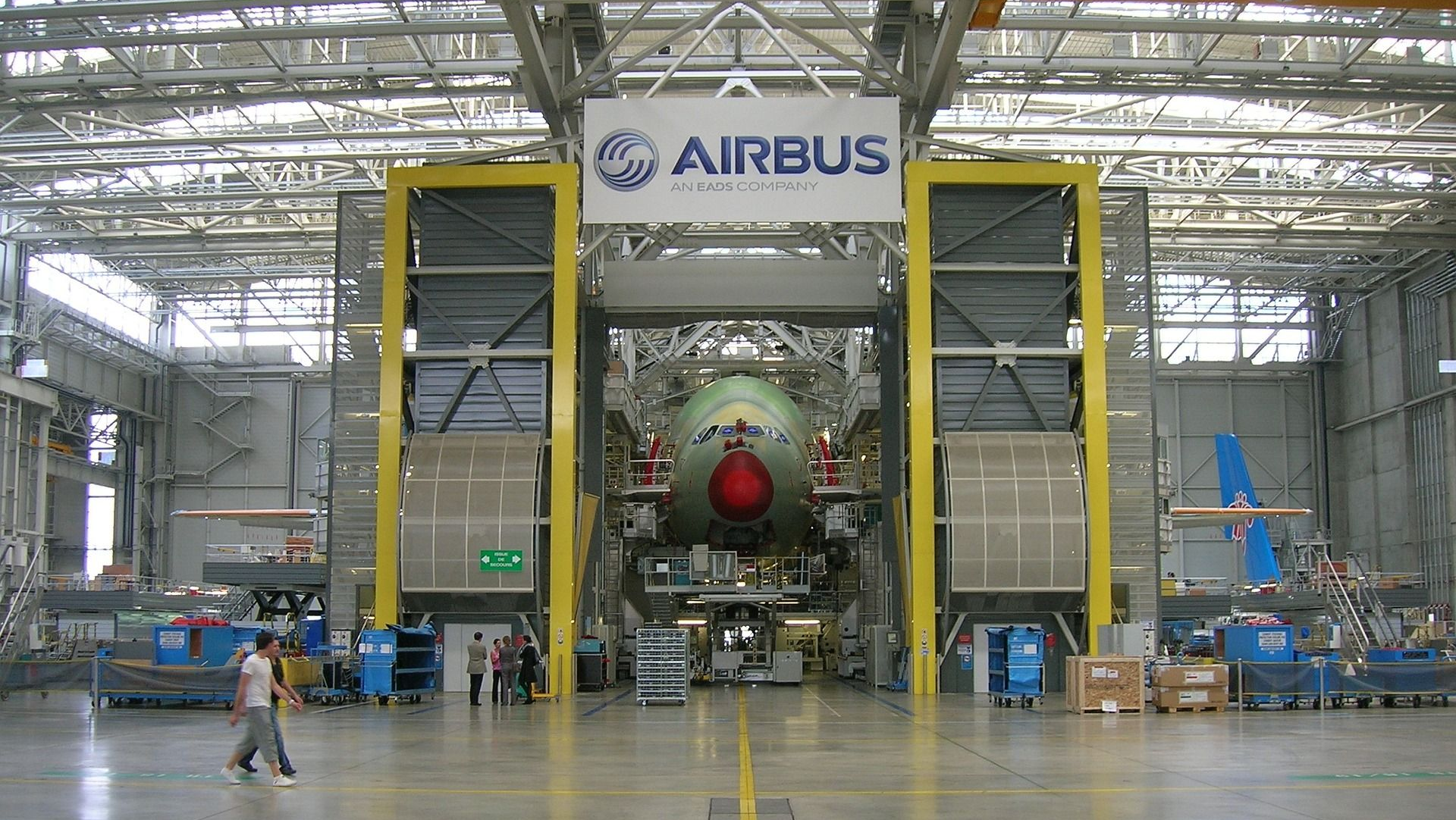 An Airbus aircraft fuselage inside a factory. People are working, the logo is visible.