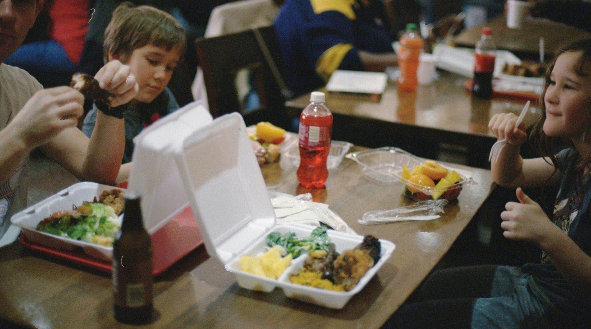 A group of people are sitting at a table eating food from styrofoam containers.
