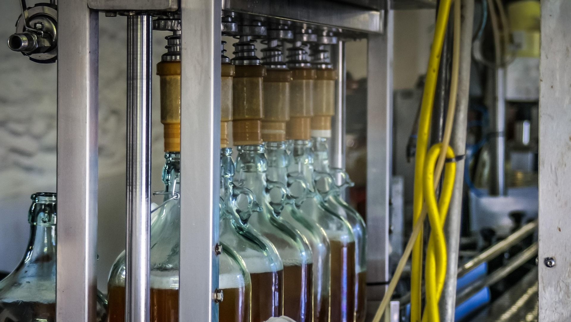 Bottling machine filling glass bottles with amber liquid in a factory setting.