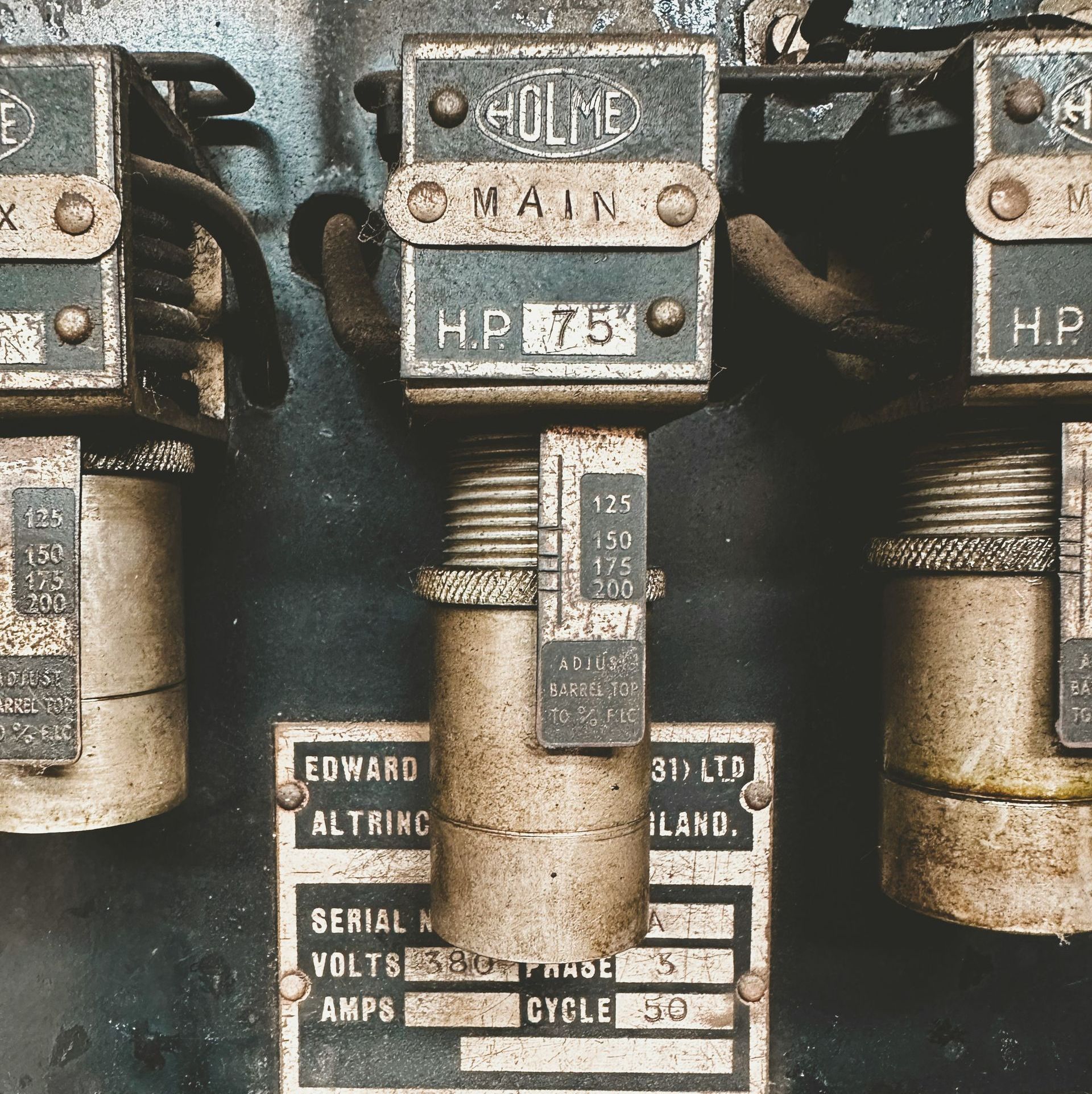 Close-up of an old electrical panel with metal boxes, labels, and wires, showing 