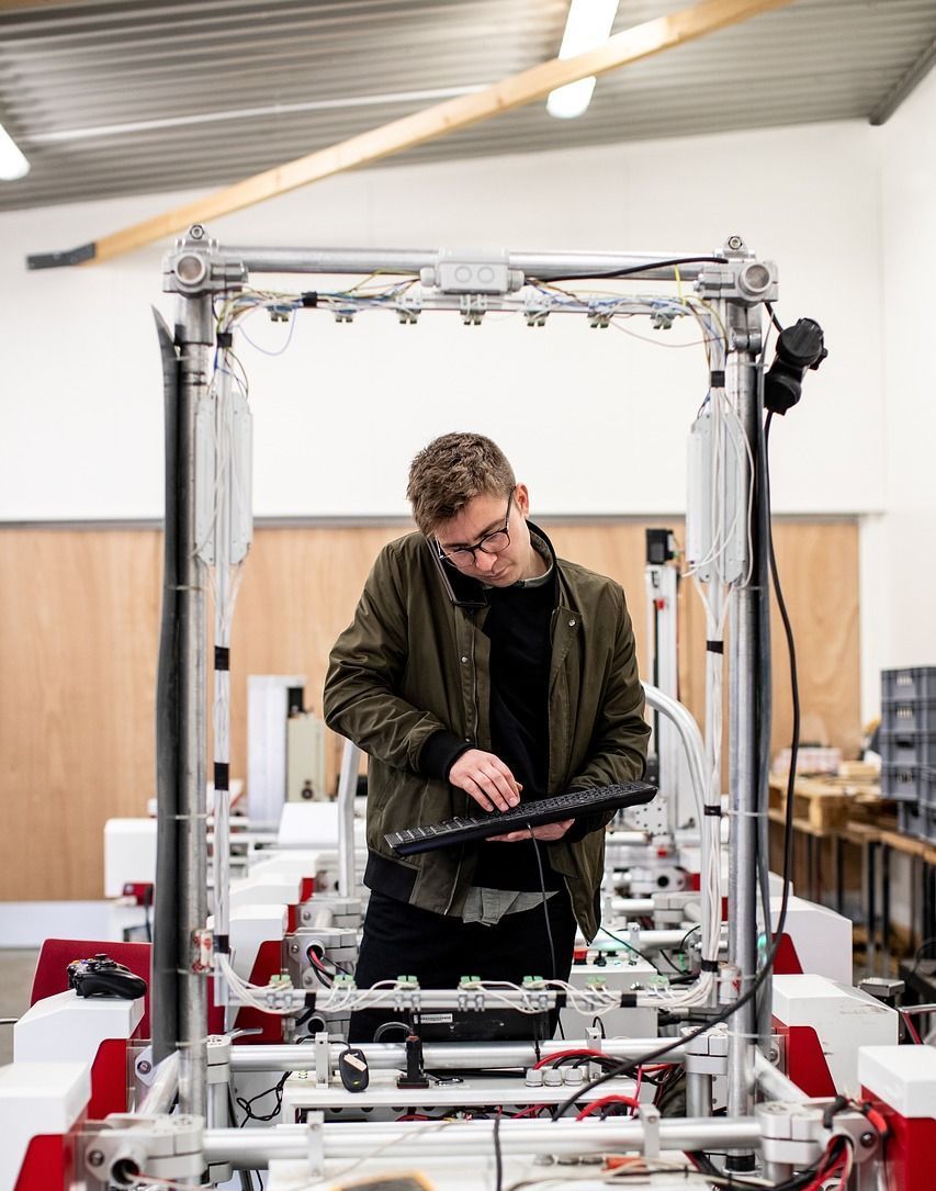 Man with glasses and a jacket working on a machine with a keyboard in a workshop.