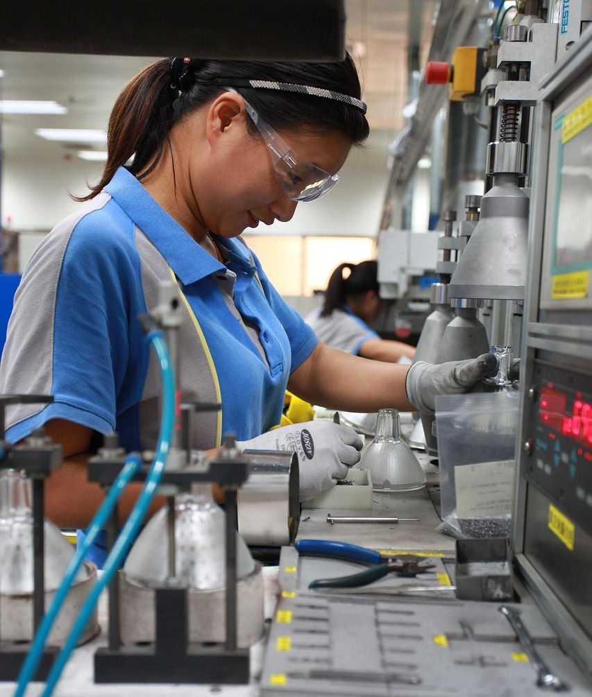 Woman in safety glasses working on an assembly line, focused, wearing gloves.