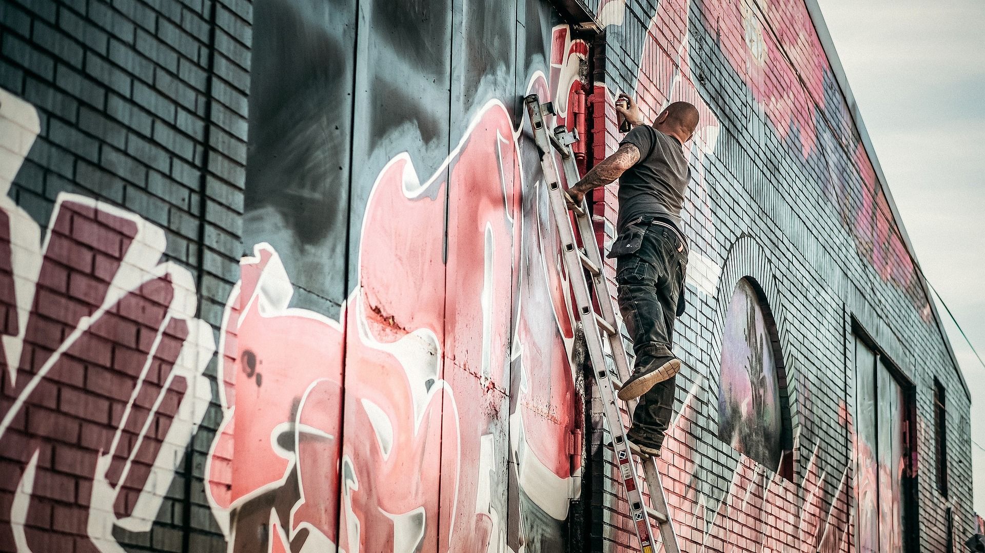 A man is painting graffiti on the side of a brick building.