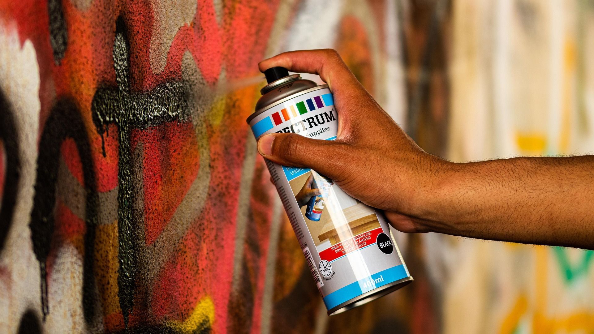 A person is spray painting graffiti on a wall with a can of spray paint.