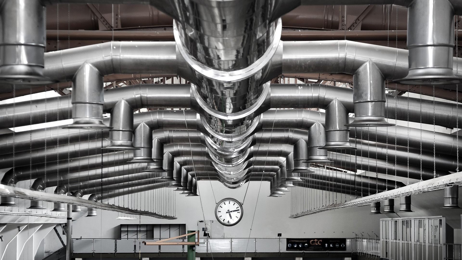 Industrial ceiling with ventilation pipes, clock, and hanging lights.