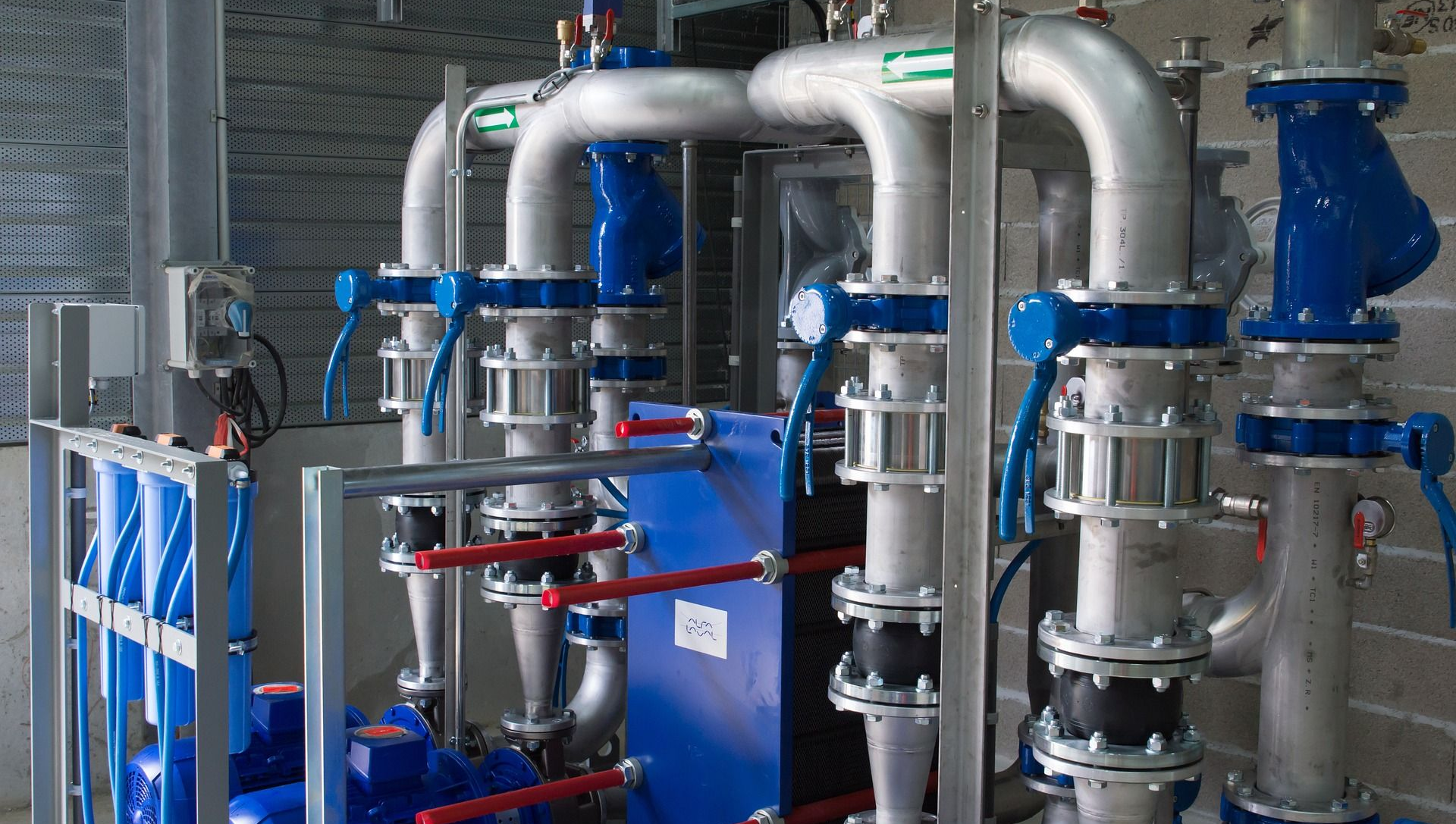 Pipes and valves in a mechanical room. Silver pipes, blue valves, blue equipment, and a gray metal frame.