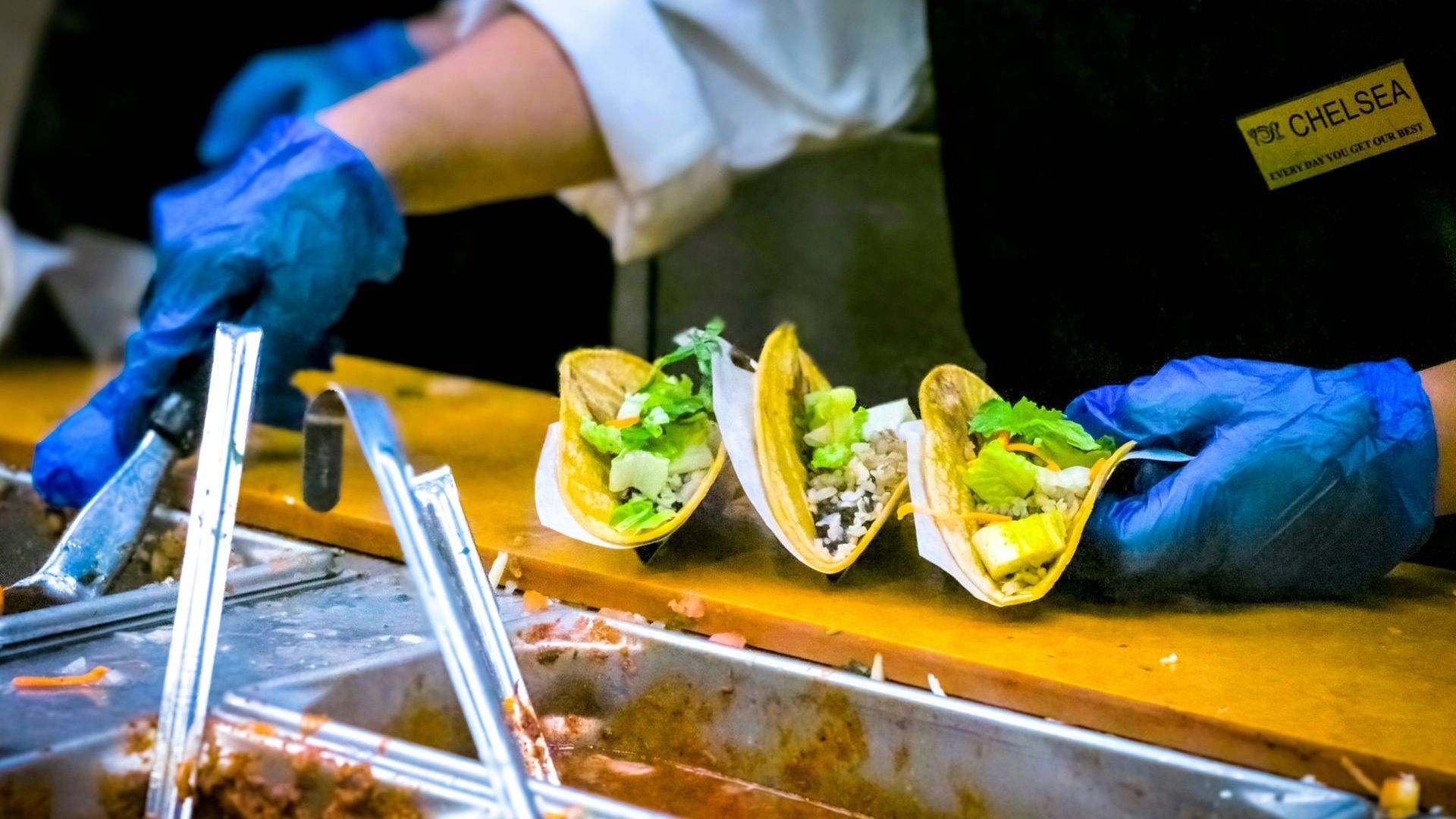 A person wearing blue gloves is cutting tacos on a cutting board.