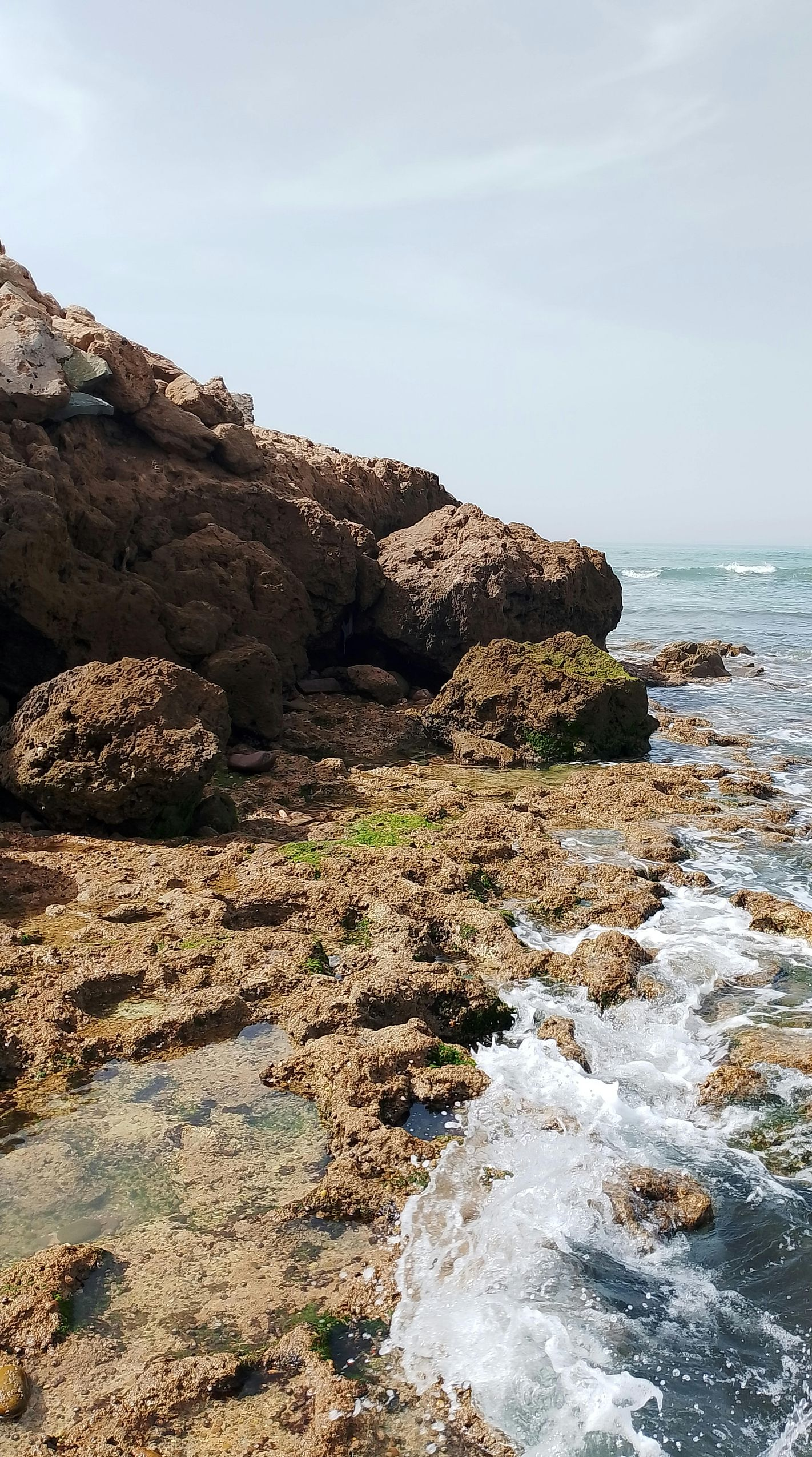 Rocky shoreline with waves crashing, clear blue sky overhead.