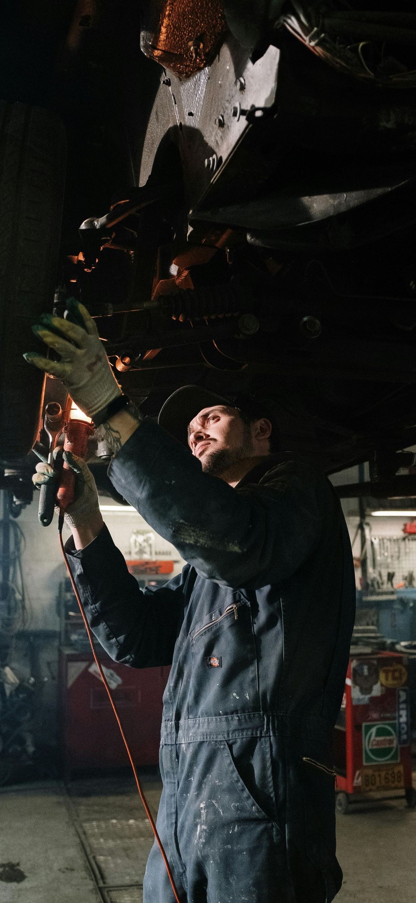 A man is welding under a car in a garage.