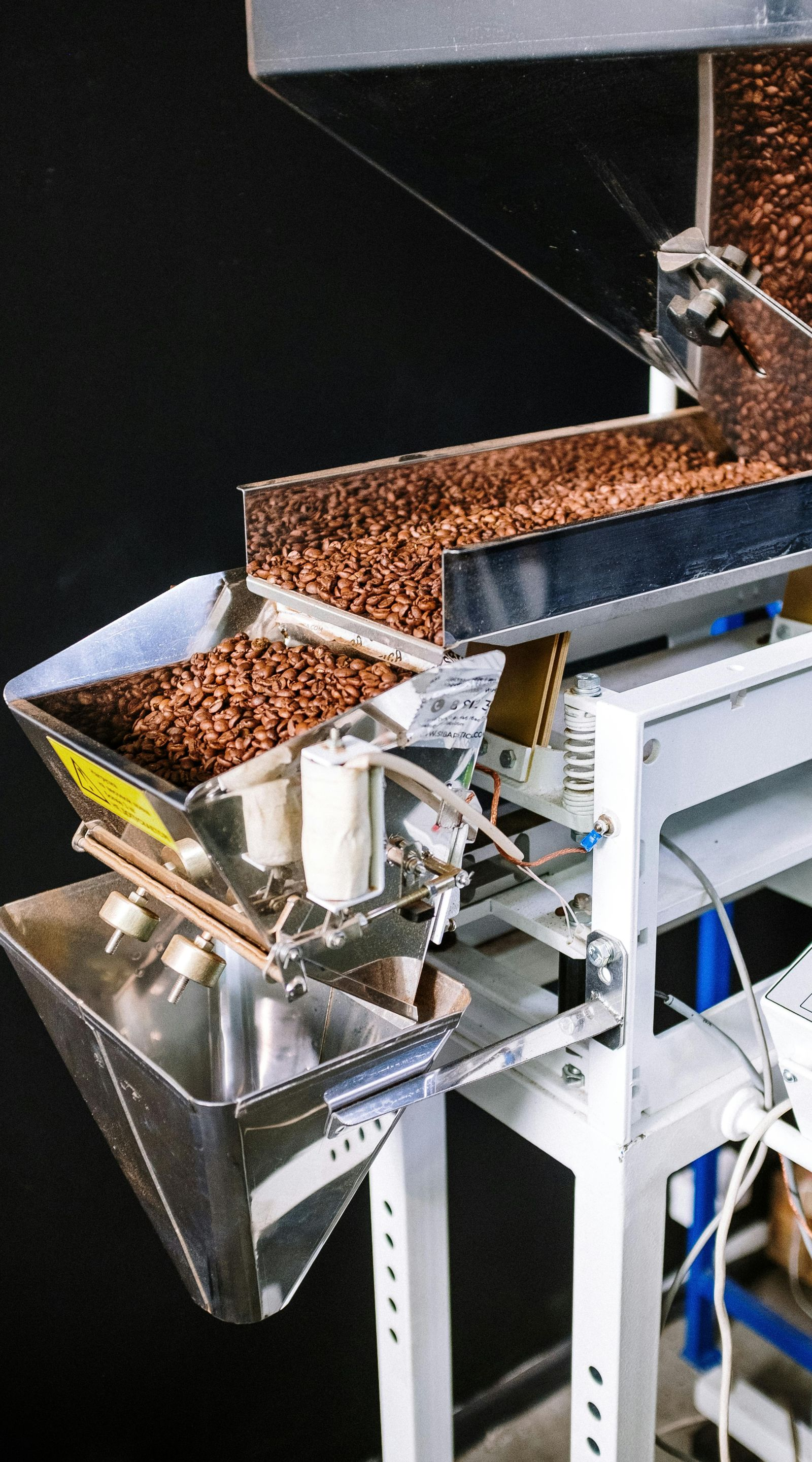A machine sorting brown peanuts into a funnel, with metal trays and support beams.