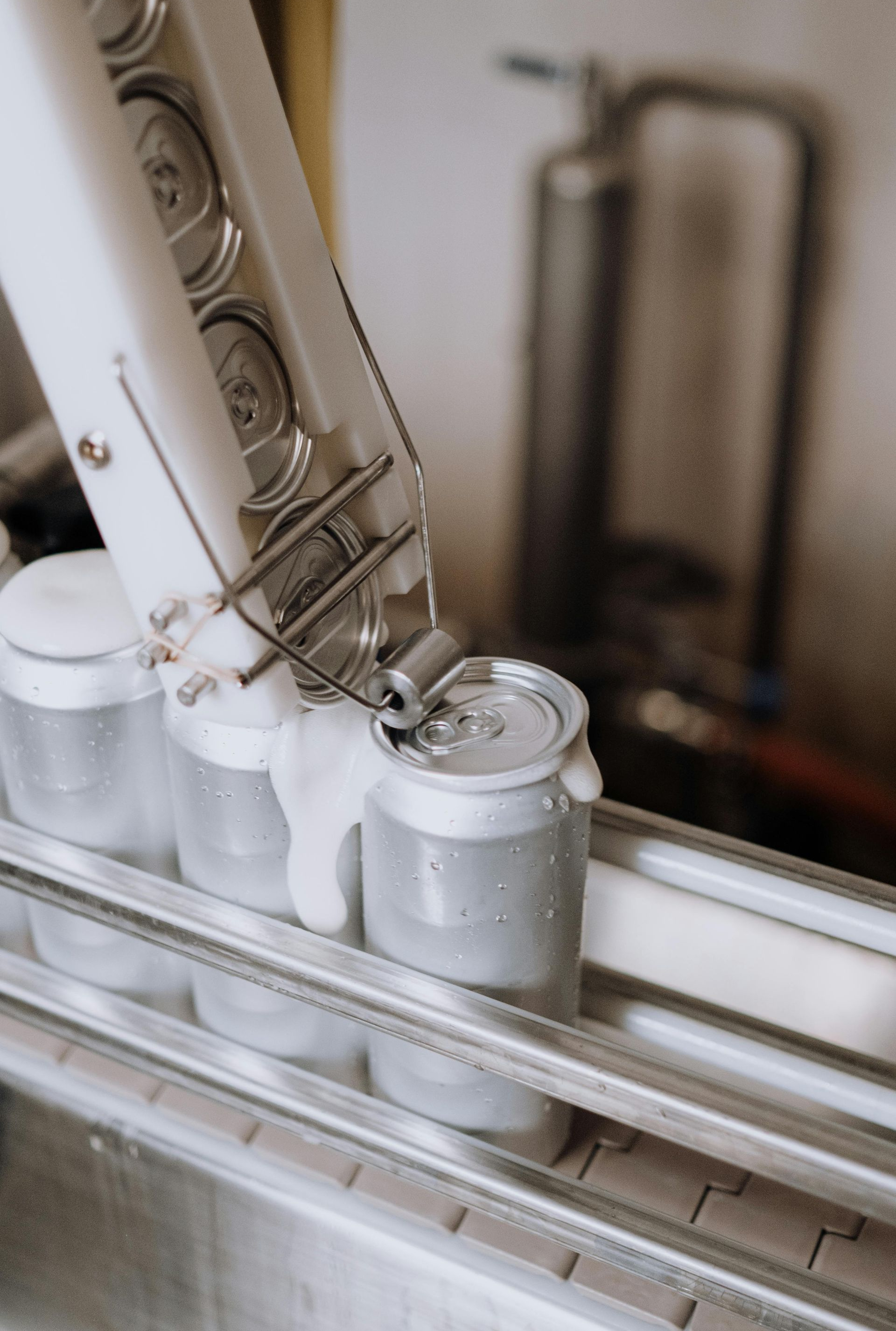 Canning machine sealing metal cans on a conveyor belt in a factory setting.