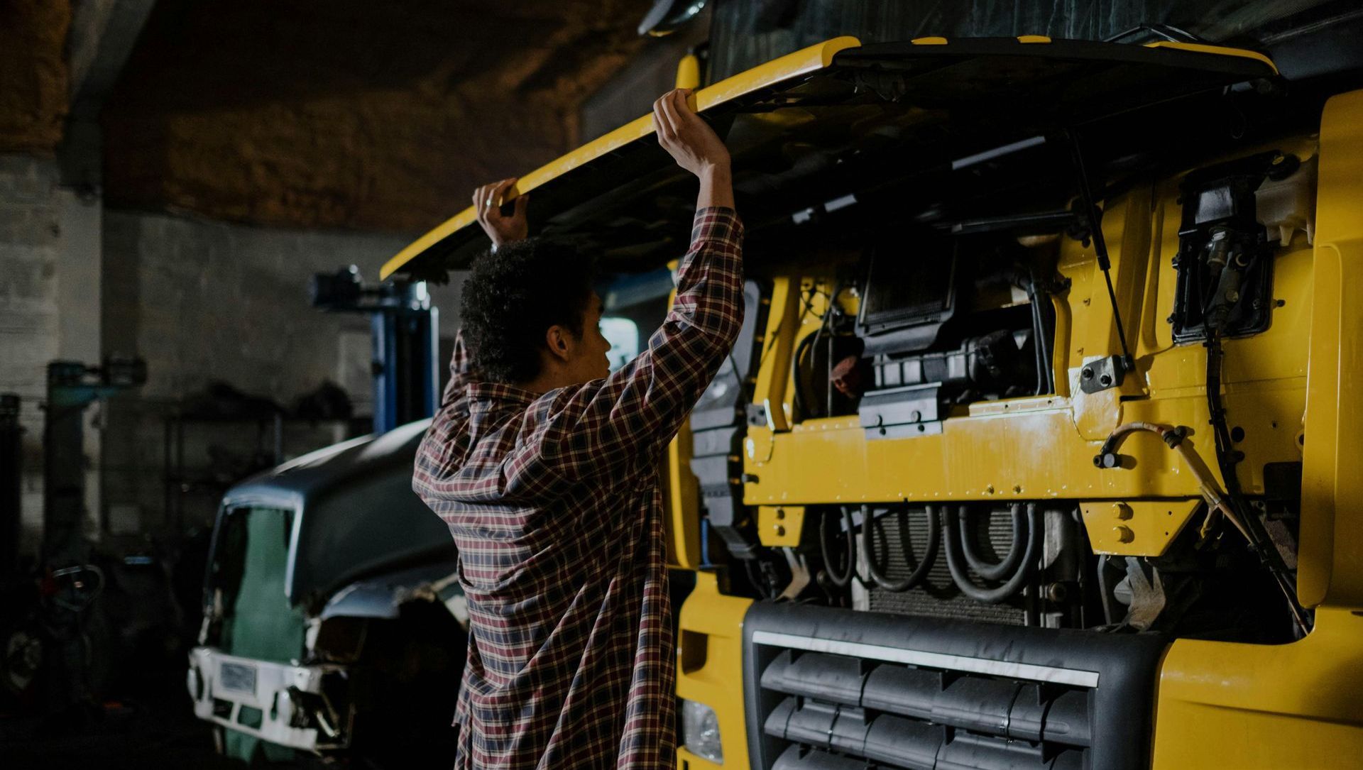 A man is lifting the hood of a truck in a garage.