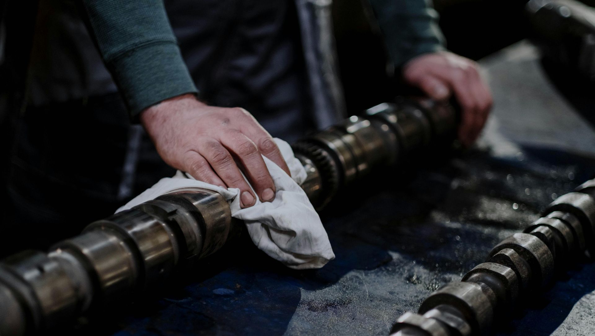 A man is cleaning a camshaft with a towel.