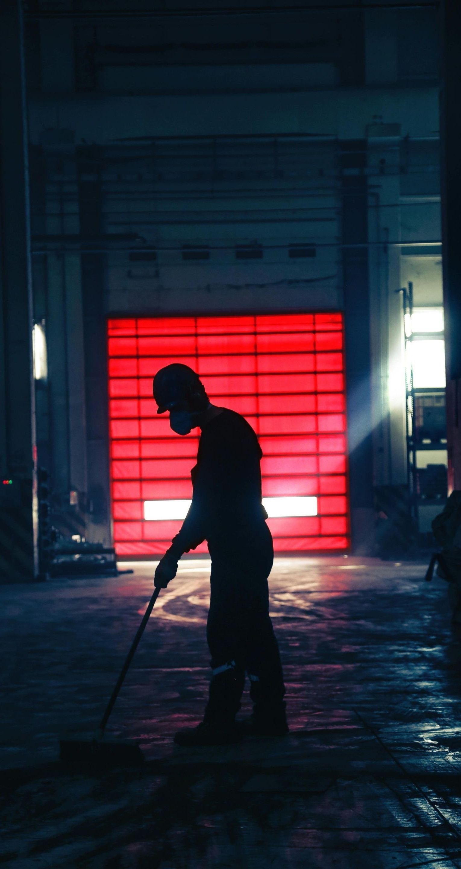 A man is sweeping the floor in a dark room with a red garage door in the background.