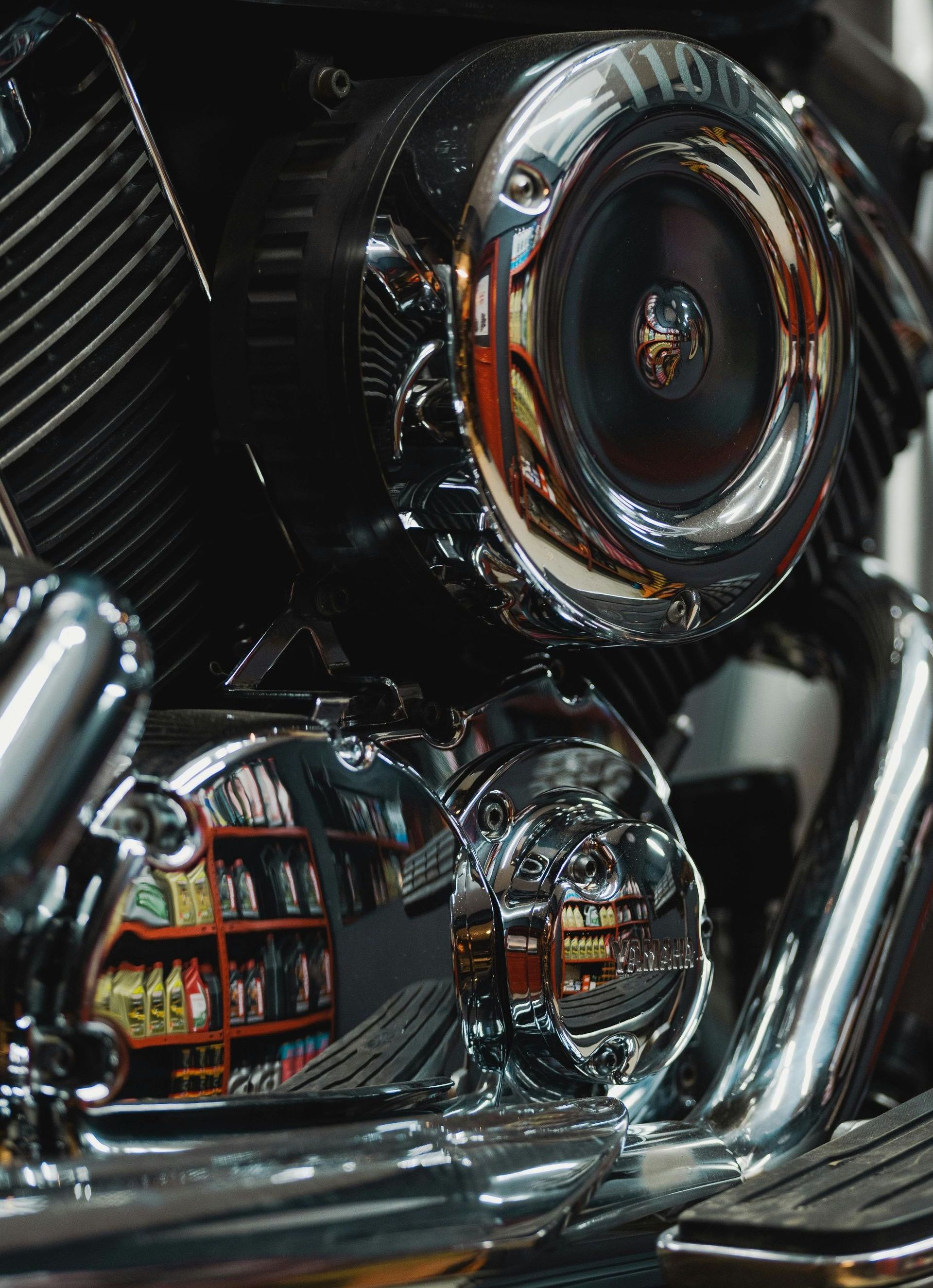 A close up of a motorcycle engine with a reflection of a store in the background.