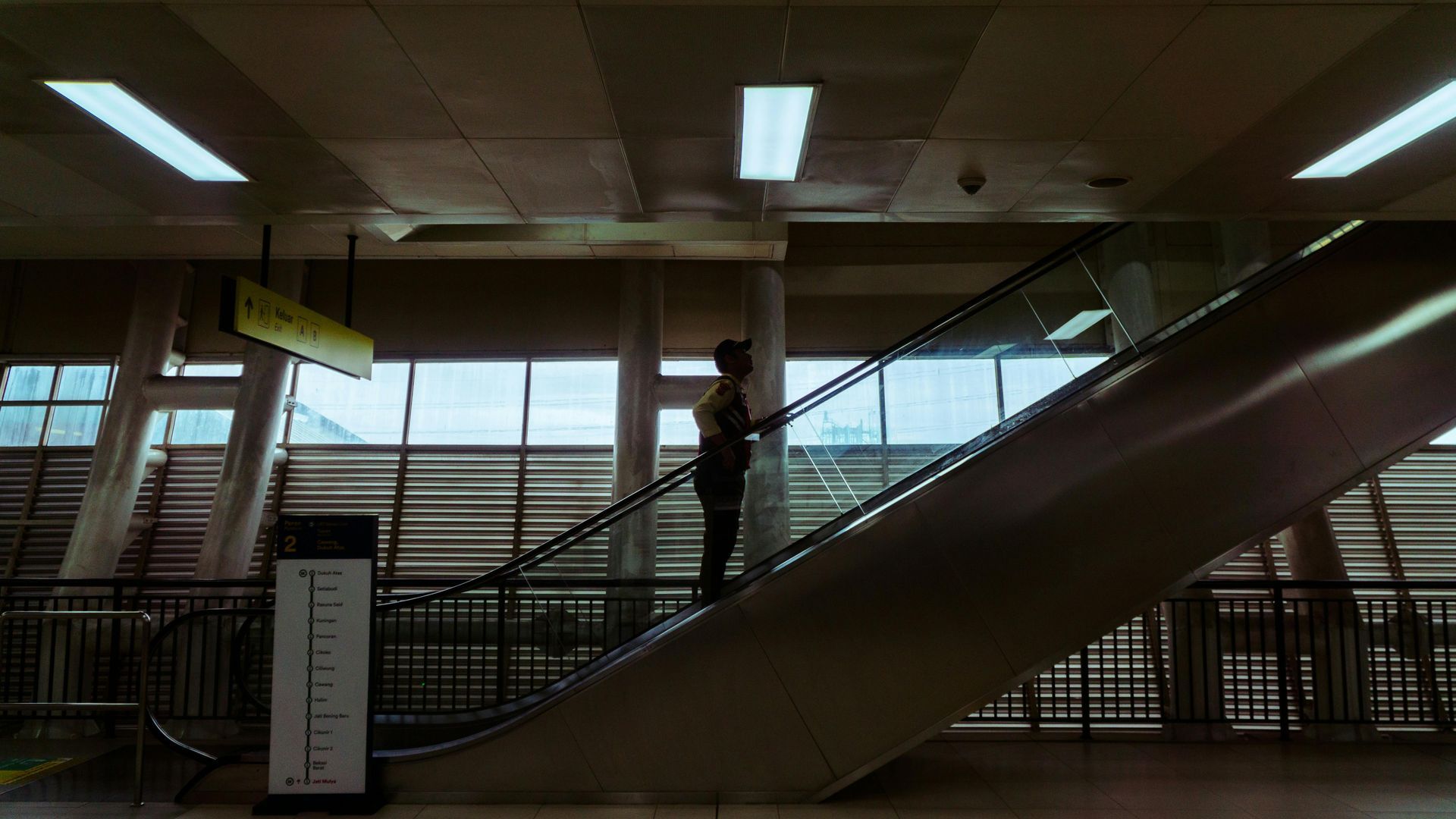 Person riding escalator up in a brightly lit, modern transit station.