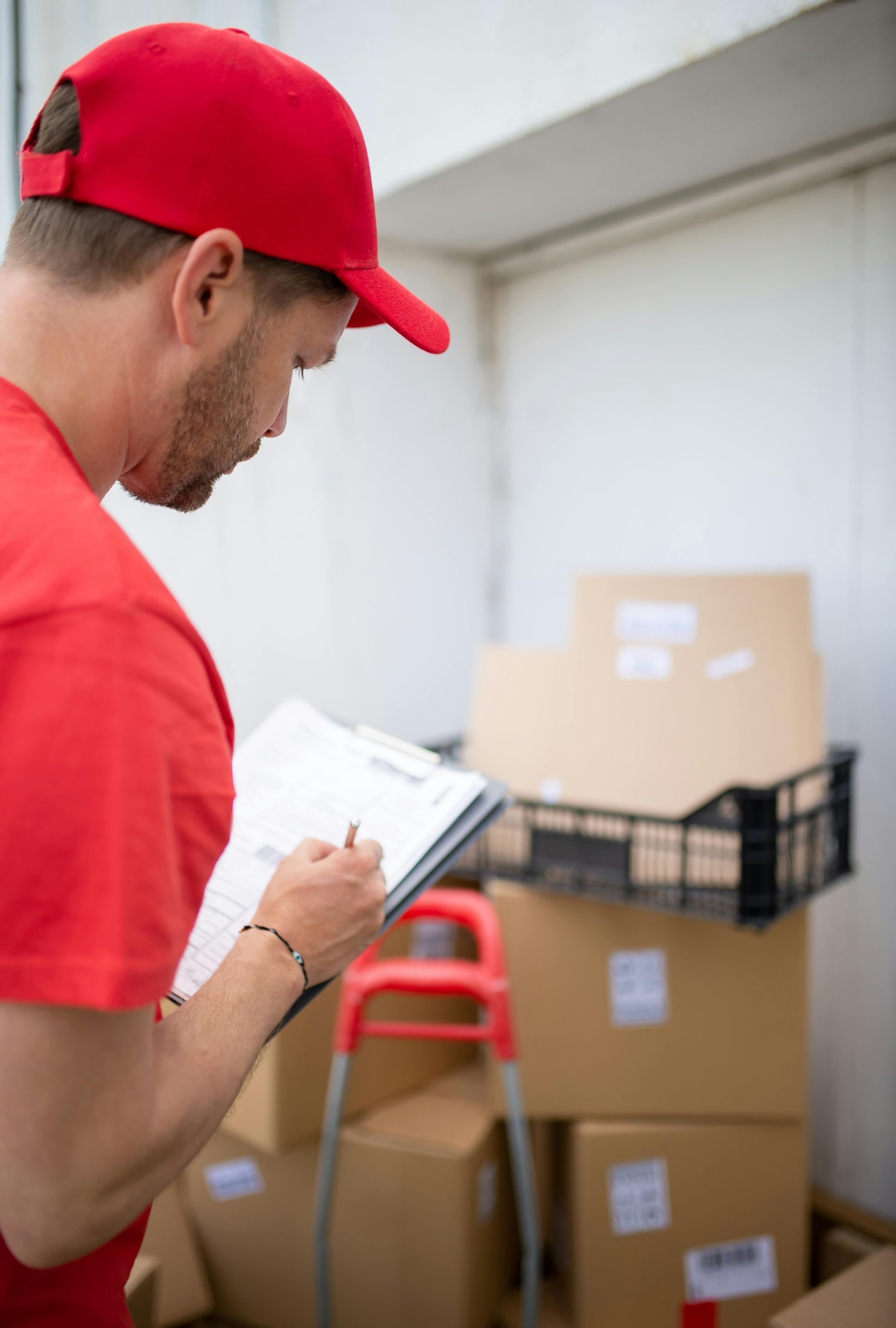 A delivery man is writing on a clipboard in front of a stack of cardboard boxes.