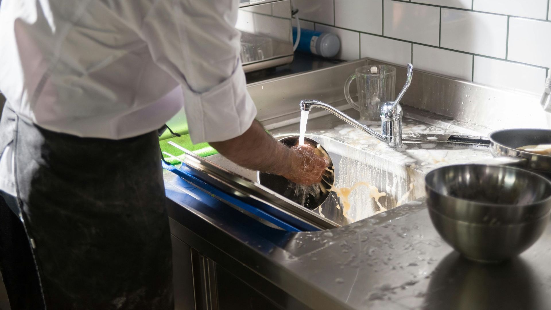 A man is washing dishes in a kitchen sink.