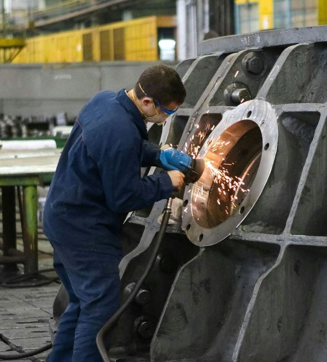 A man in a blue jumpsuit is grinding a piece of metal