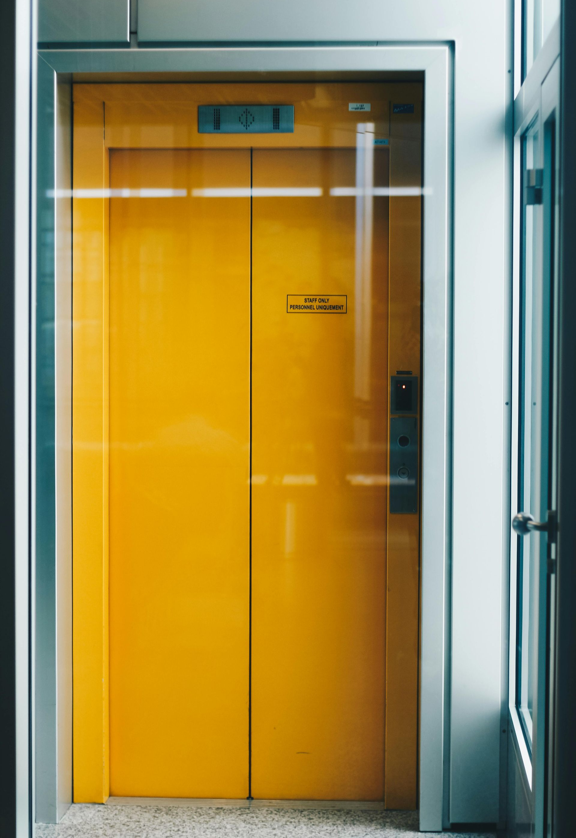 Yellow elevator doors, partially visible through a glass panel, set in a modern building.