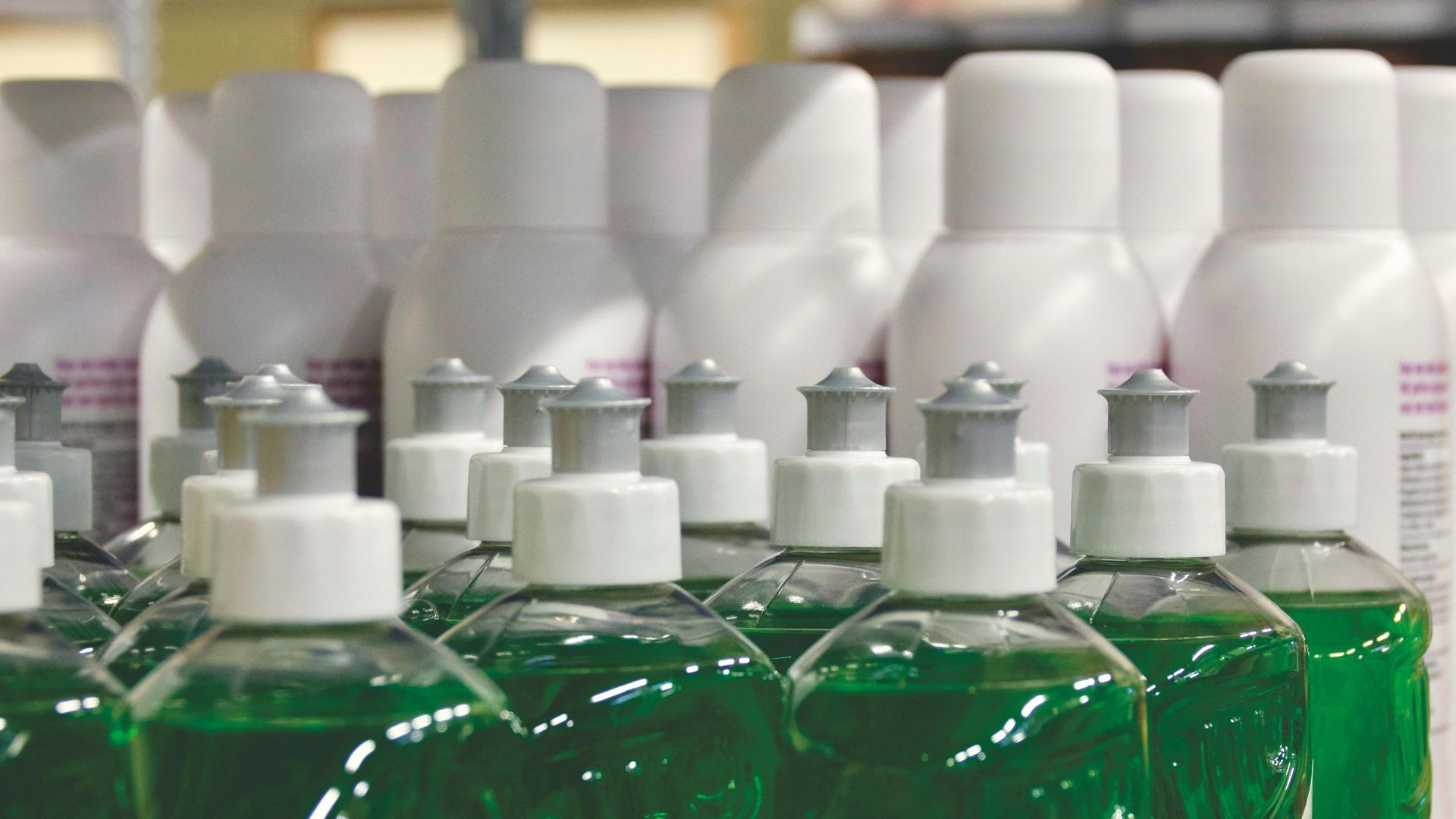 Green liquid soap bottles and white plastic bottles, presumably for lotion, on a shelf.
