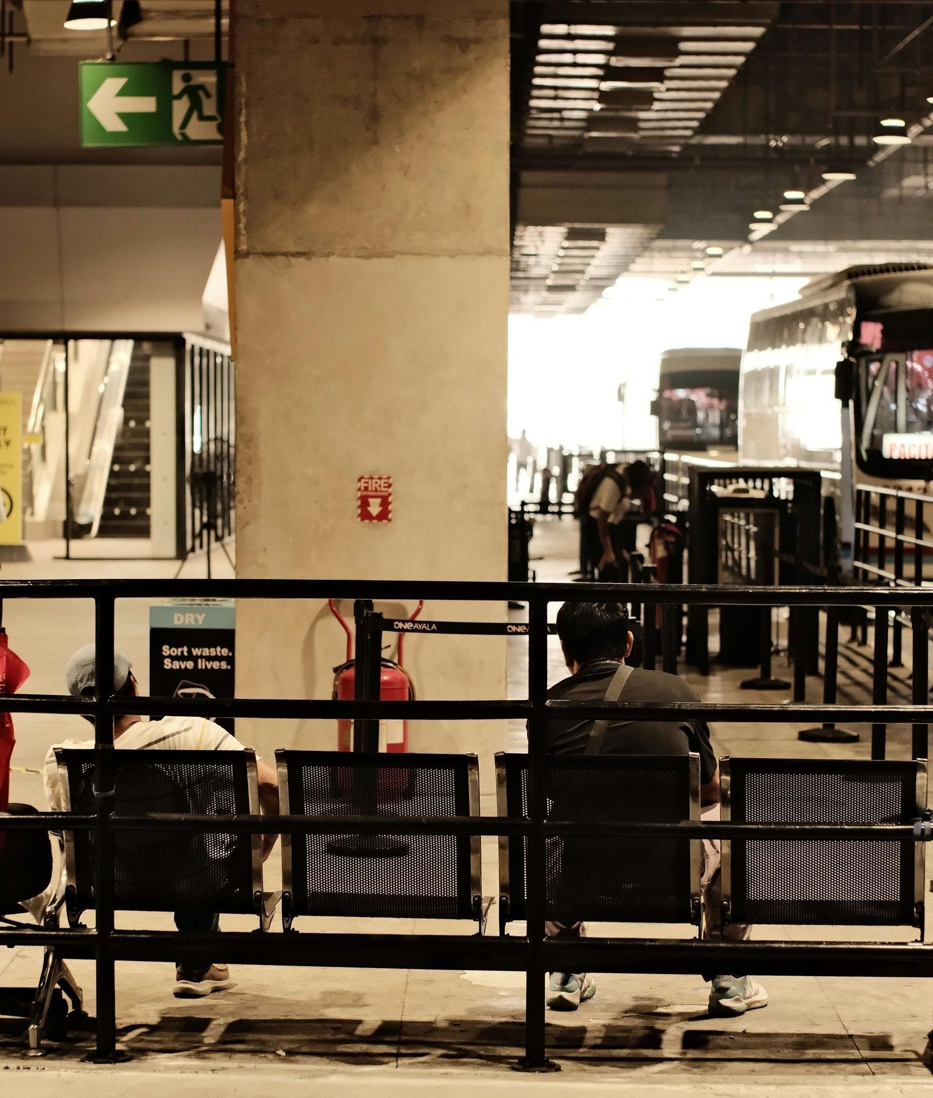 People sitting on benches in front of a green exit sign