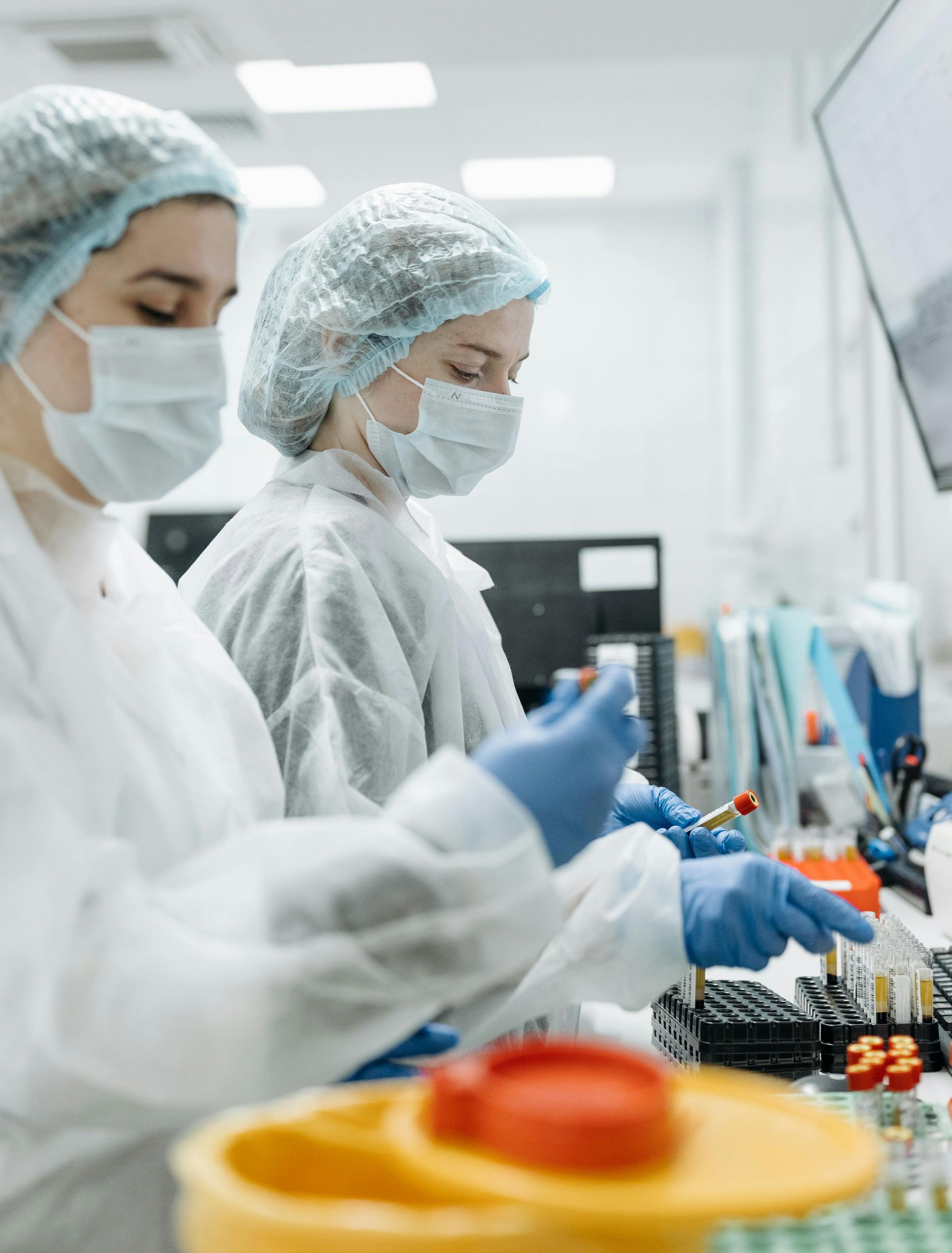 Two lab technicians in protective gear working with samples in a bright lab.