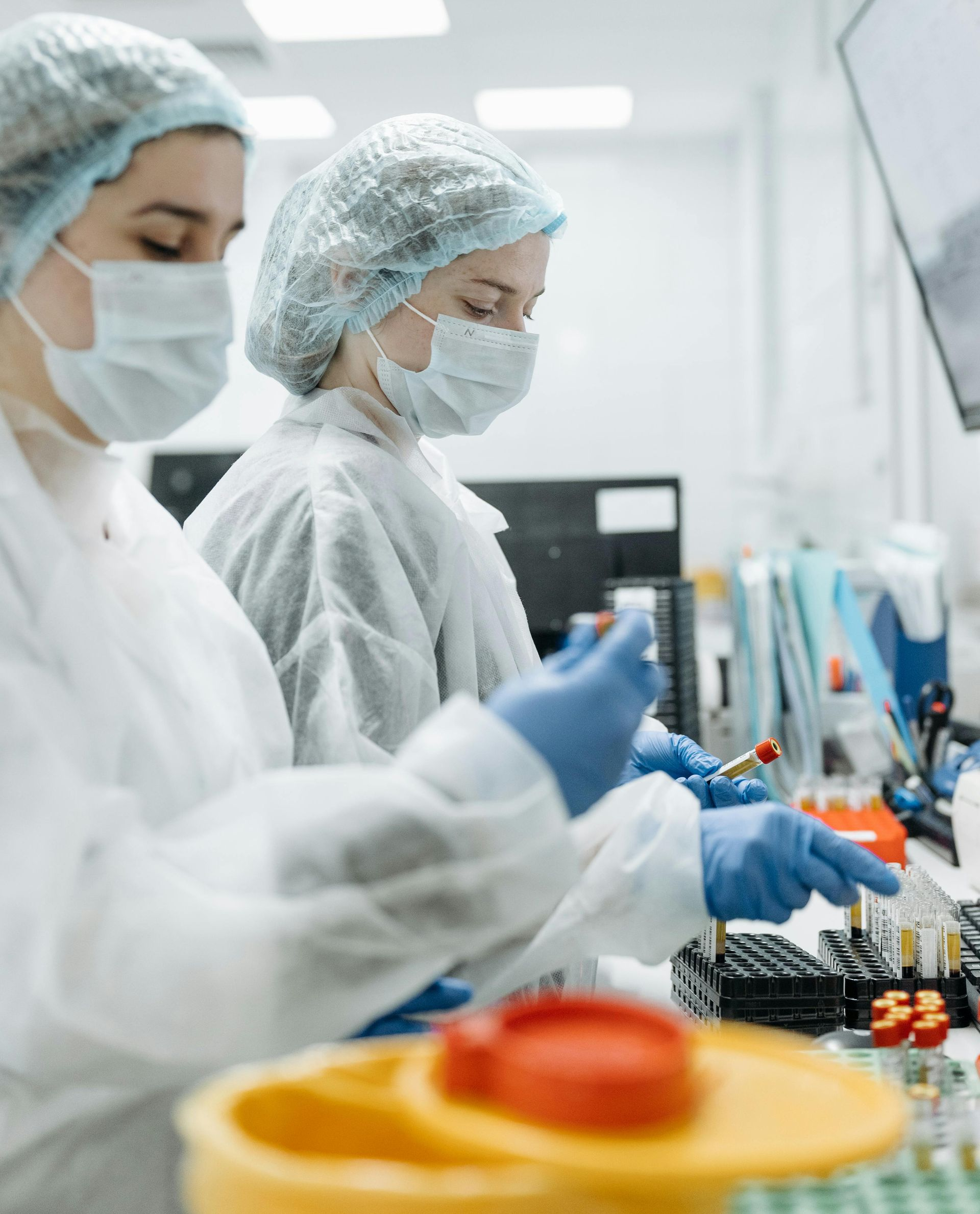 Two lab technicians in protective gear working with samples in a bright lab.