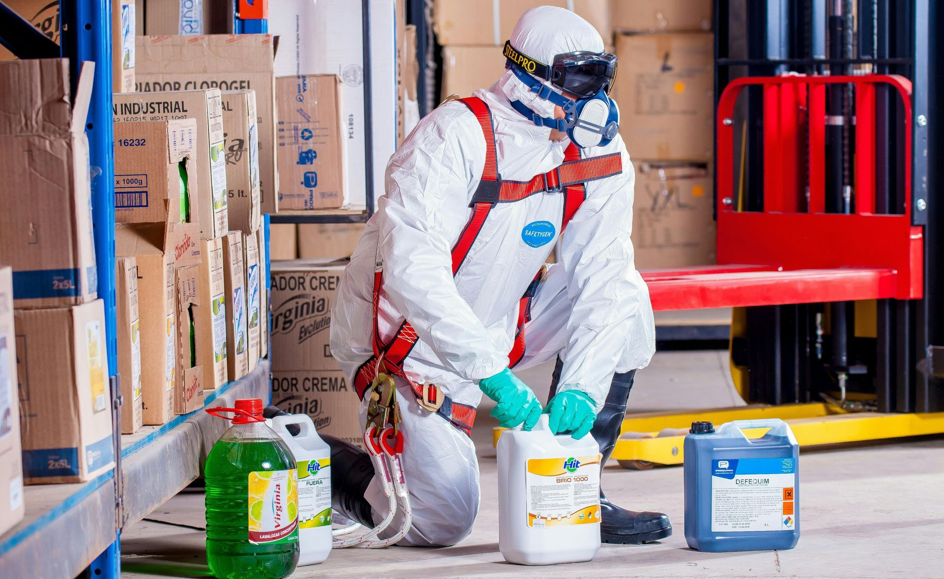 Person in hazmat suit handling chemicals in a warehouse.