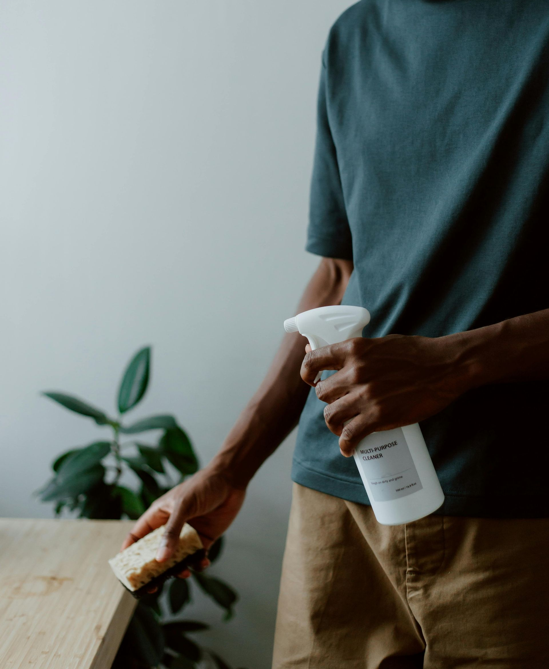 Person spraying cleaner and wiping a wooden surface with a sponge indoors.