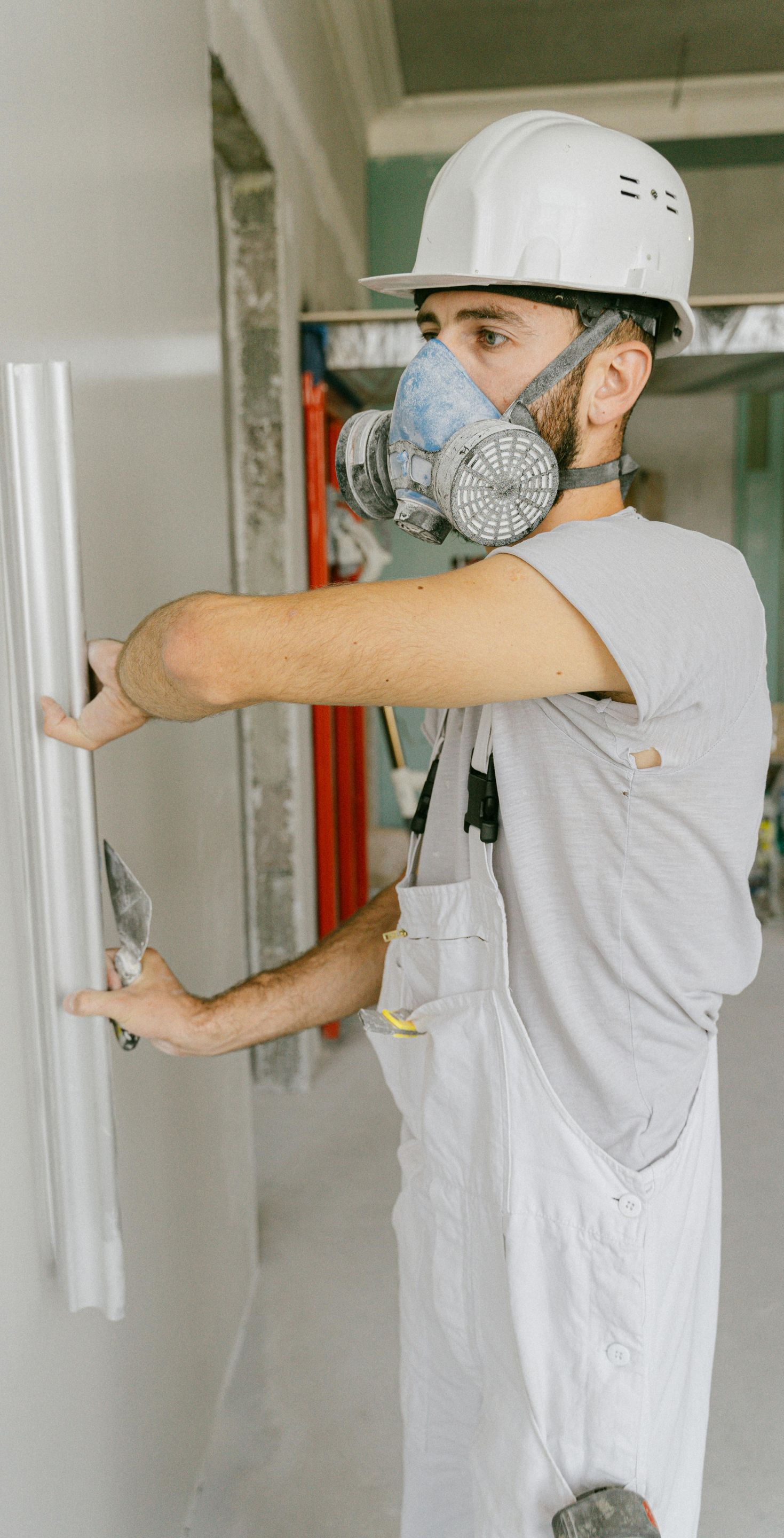 Man wearing safety gear, smoothing wall with a trowel. Construction site.