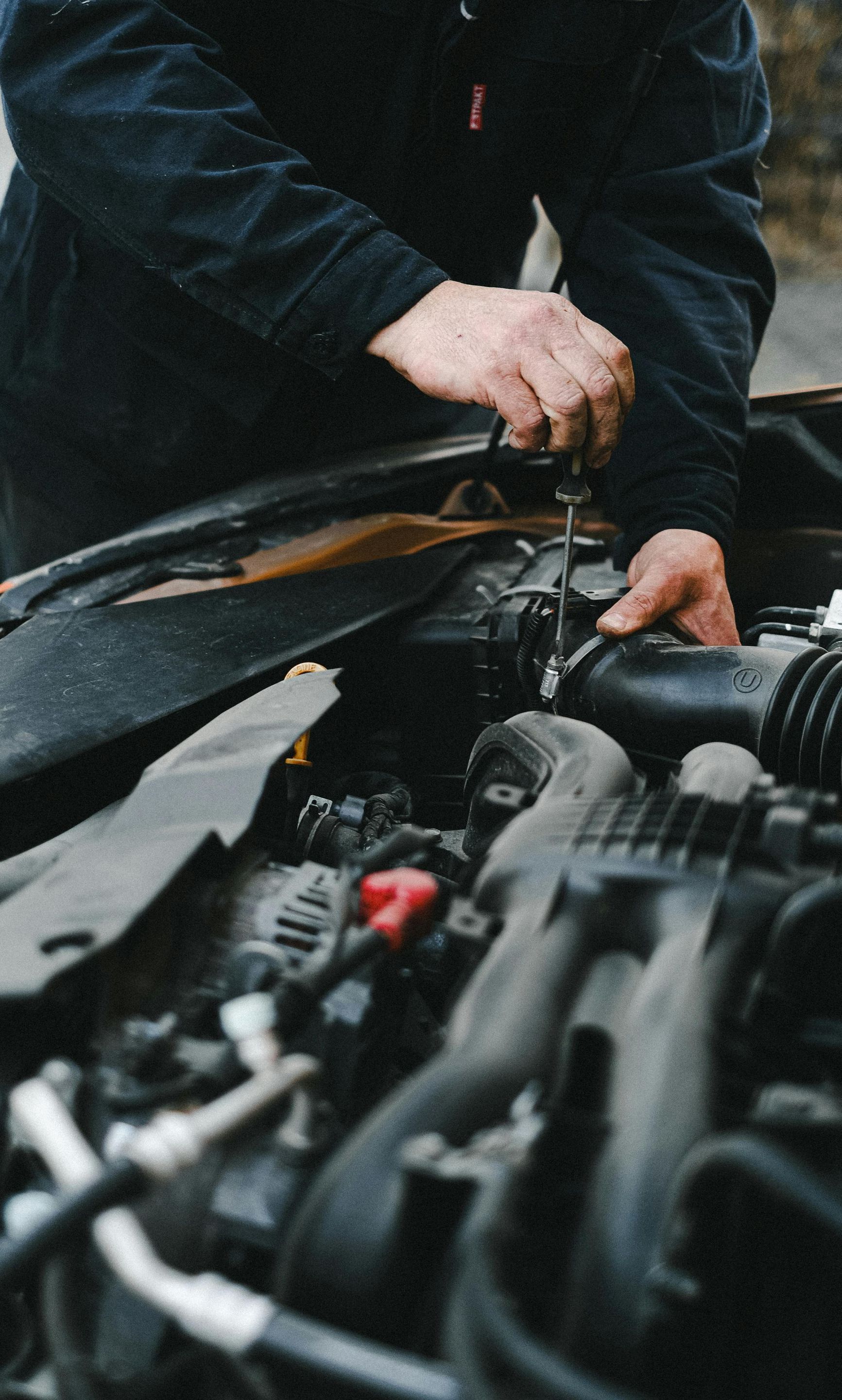 A man is working on a car engine with a screwdriver.