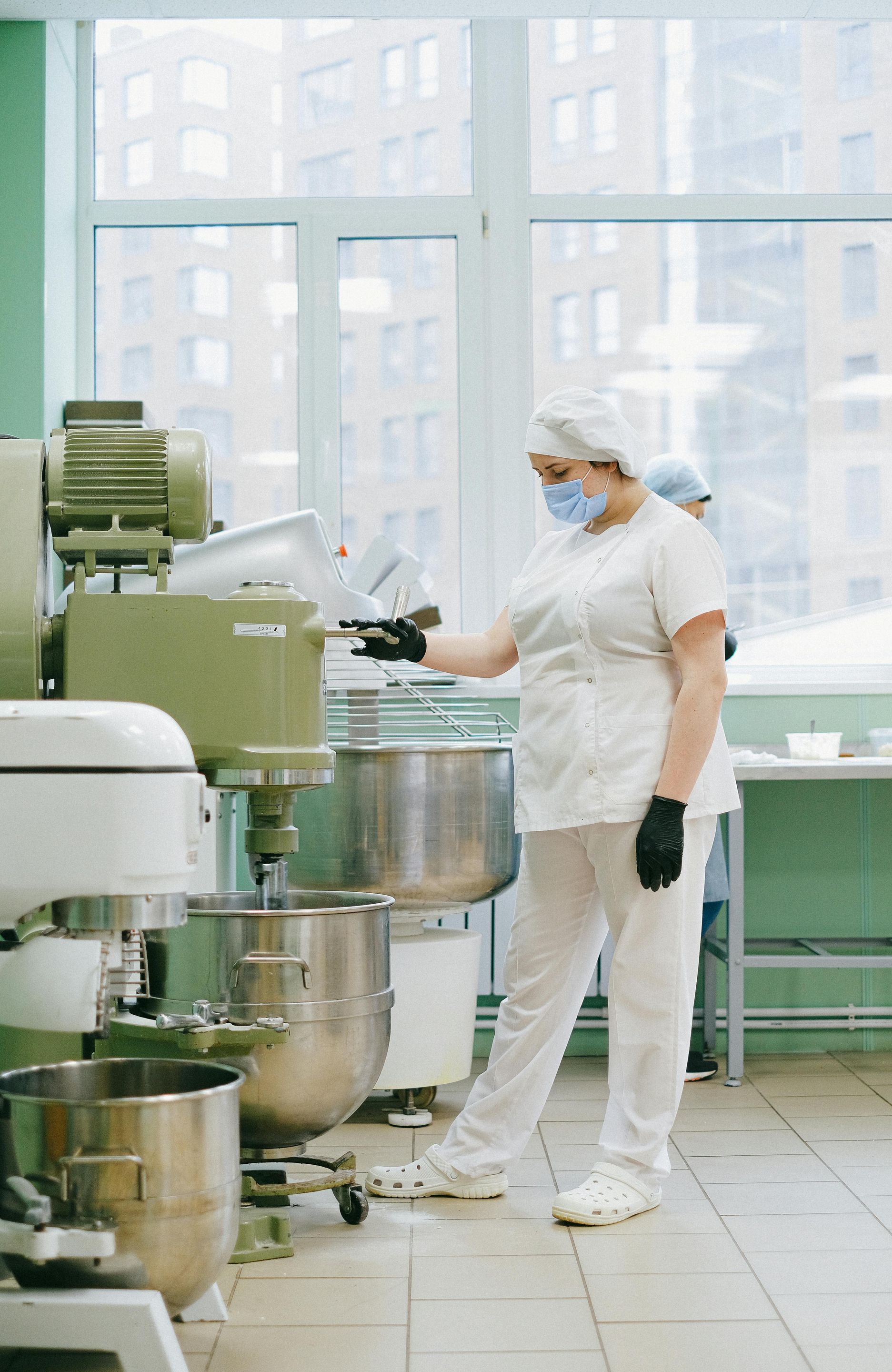 A woman wearing a mask is standing in front of a mixer in a kitchen.