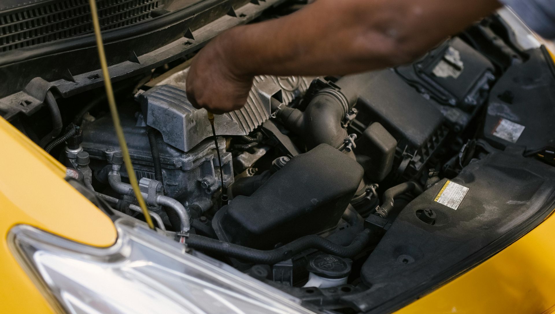 A man is looking under the hood of a yellow car.