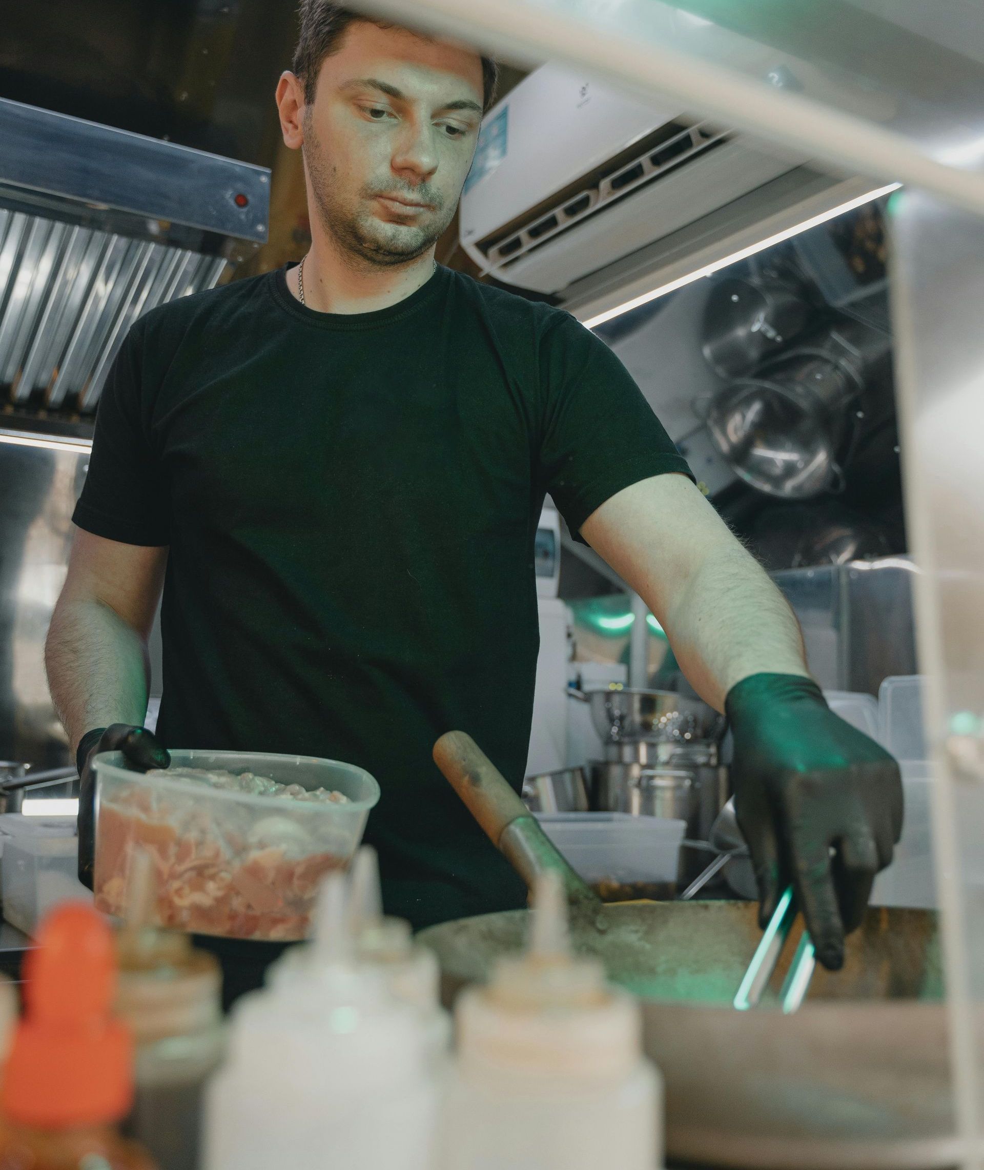 A man in a black shirt and black gloves is preparing food in a kitchen