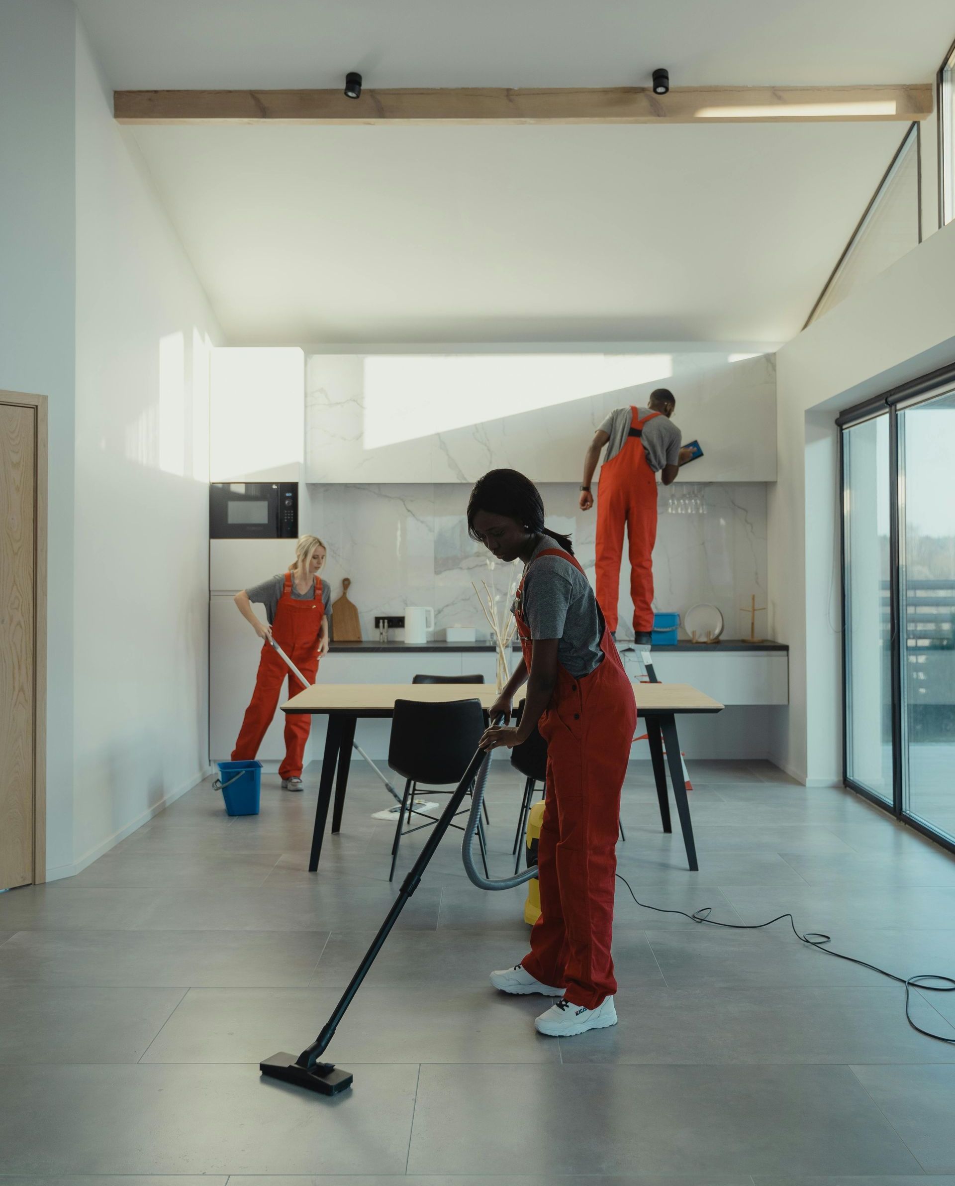 A man in red overalls is cleaning the floor with a vacuum cleaner