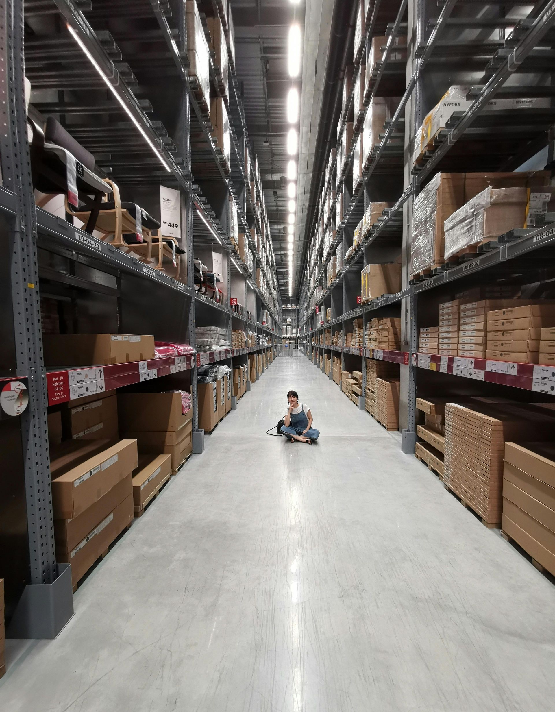 A person is sitting on the floor of a warehouse surrounded by shelves and boxes.